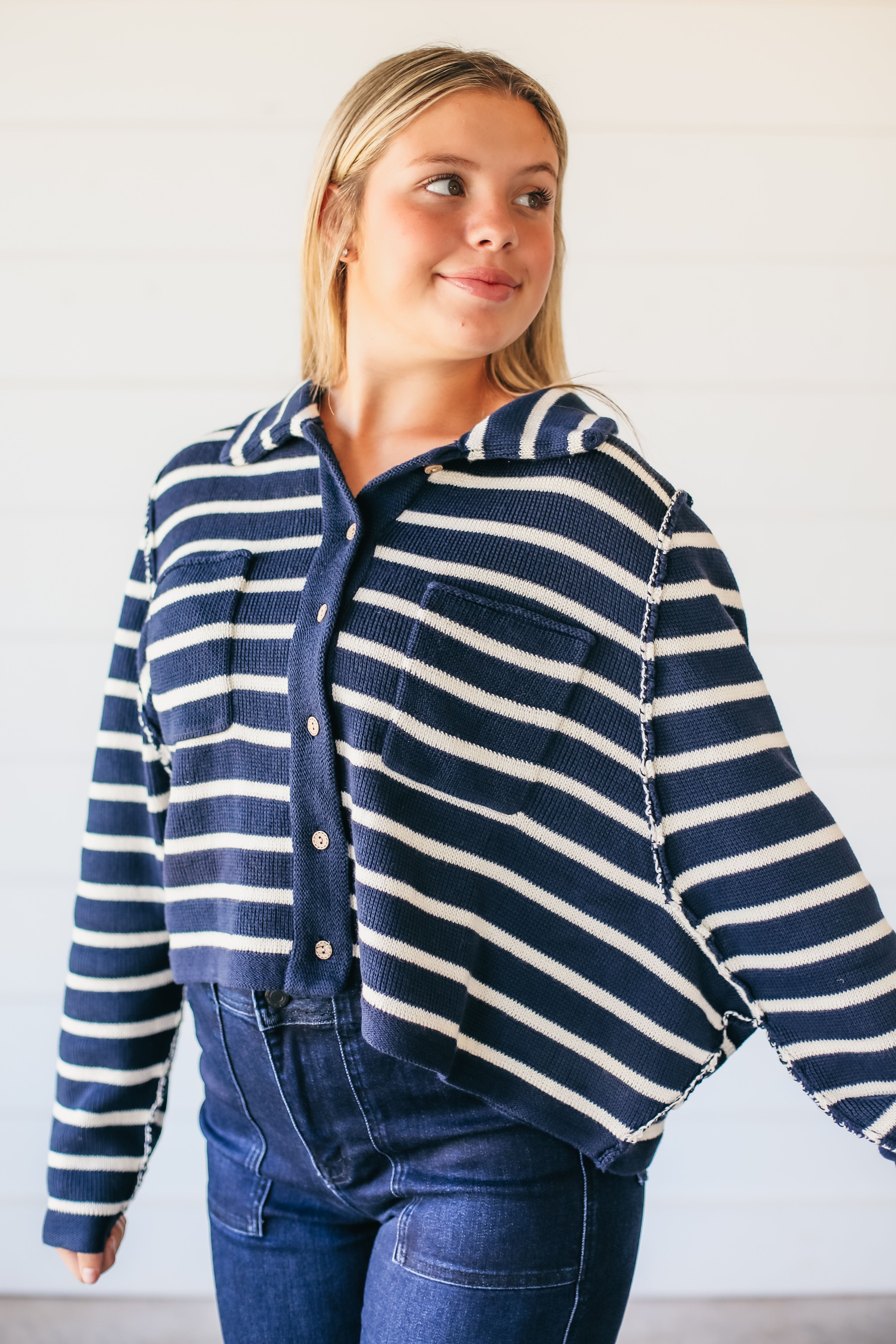 Woman wearing a navy and white striped button-down collared sweater with two chest pockets and dark wash jeans.