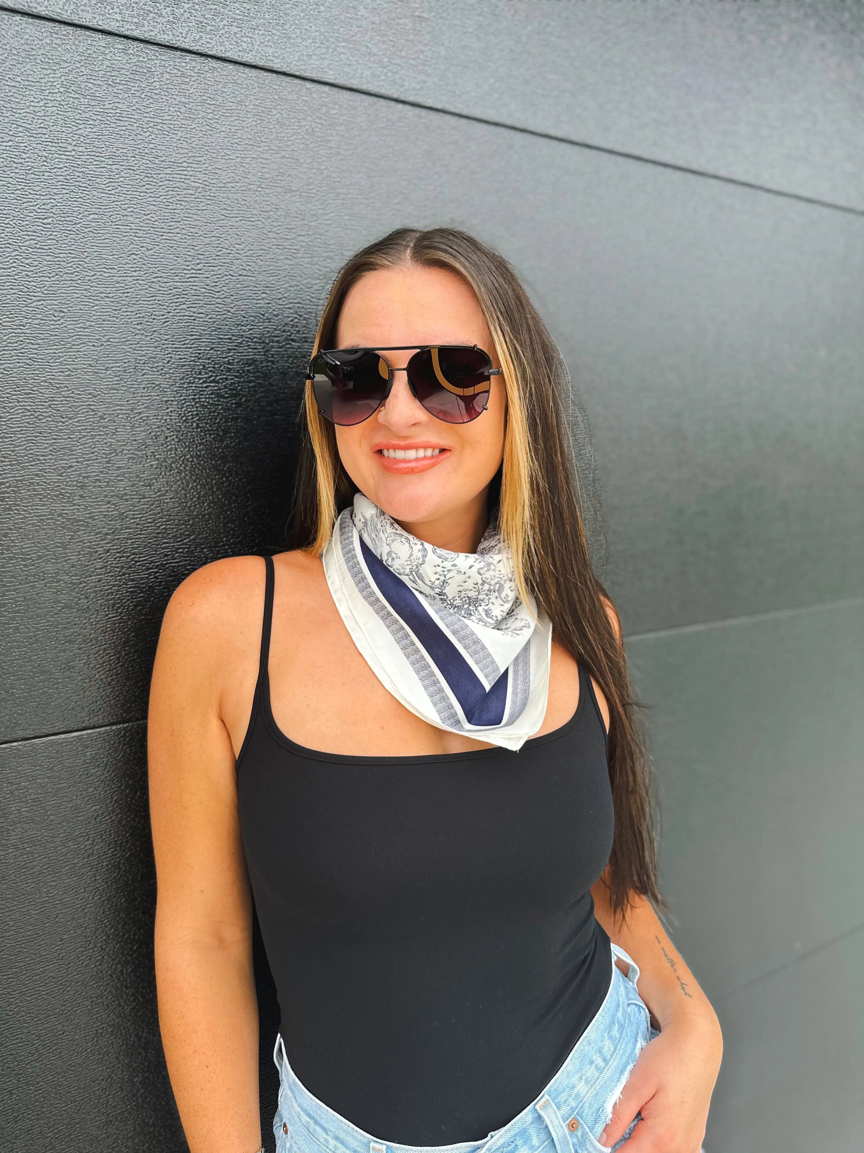 Woman wearing a navy and white toile print neck scarf with a blue and white border, black tank top, and sunglasses.