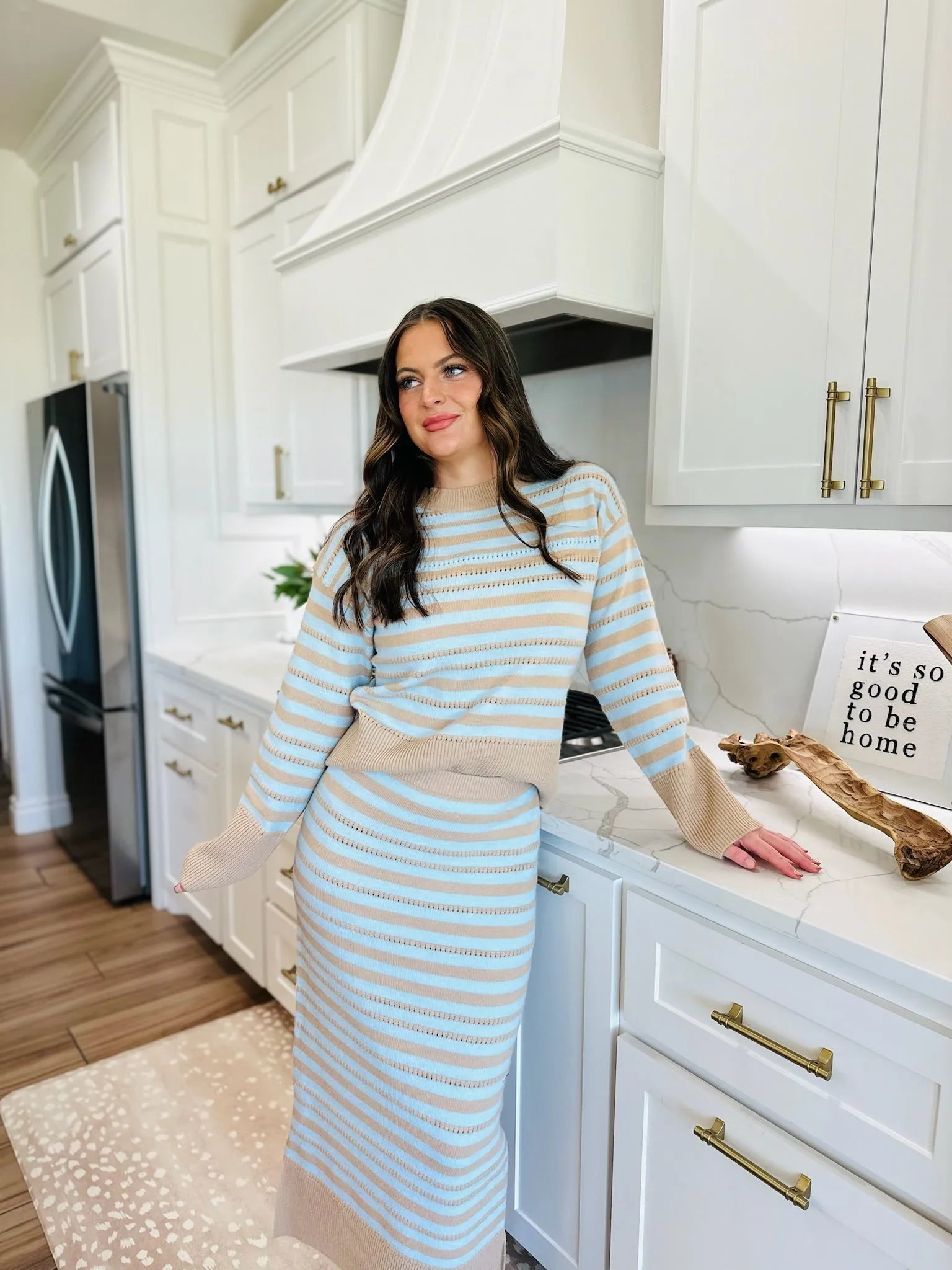 Woman wearing a blue and oatmeal striped knit sweater and matching skirt, in a modern kitchen.