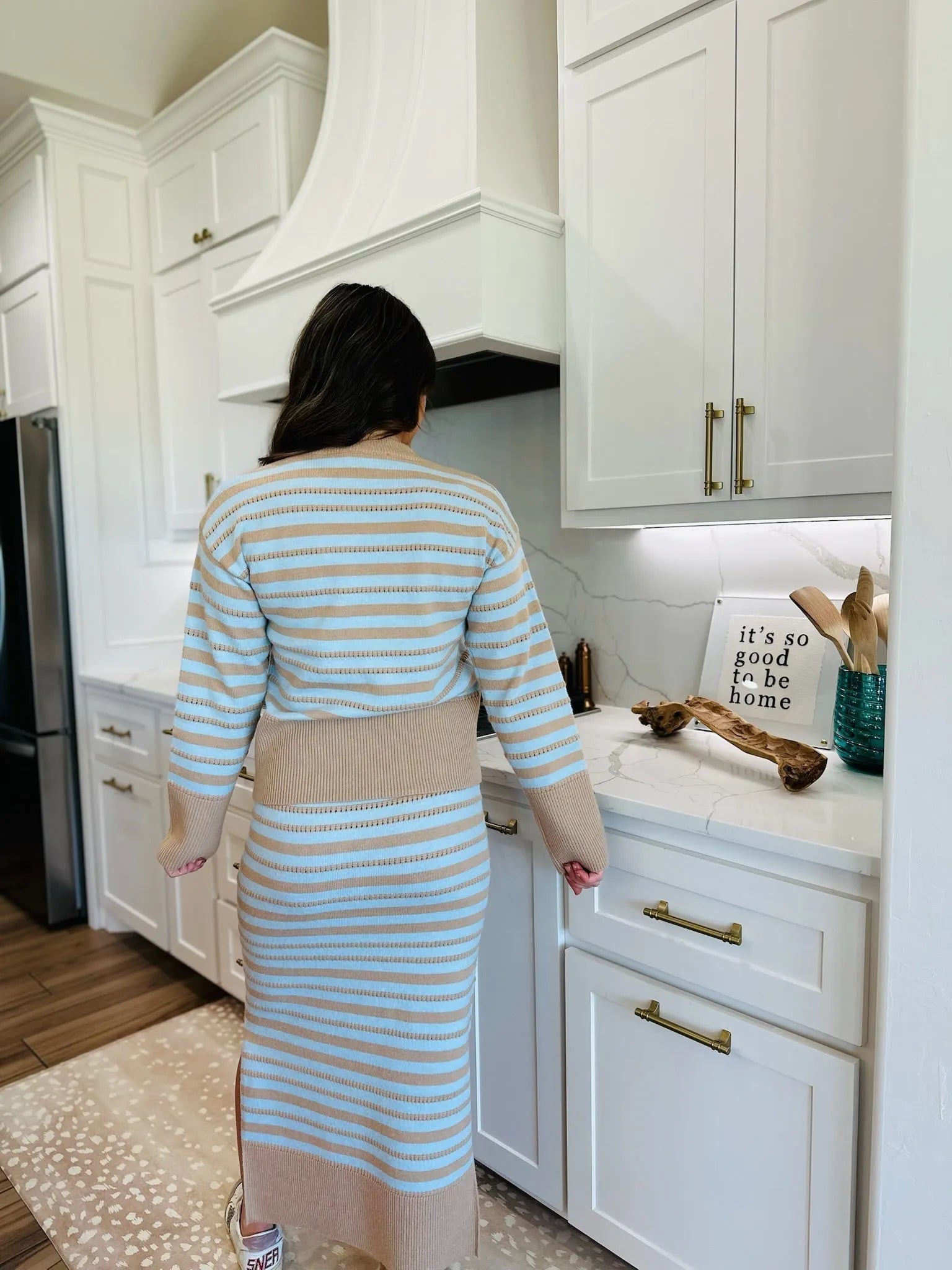 Woman in oatmeal and blue striped matching sweater and skirt set in a modern kitchen.