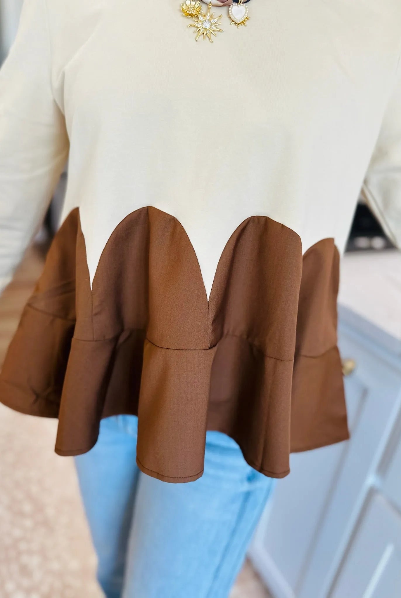 Oatmeal knit top with brown ruffled peplum detail and scalloped hem.