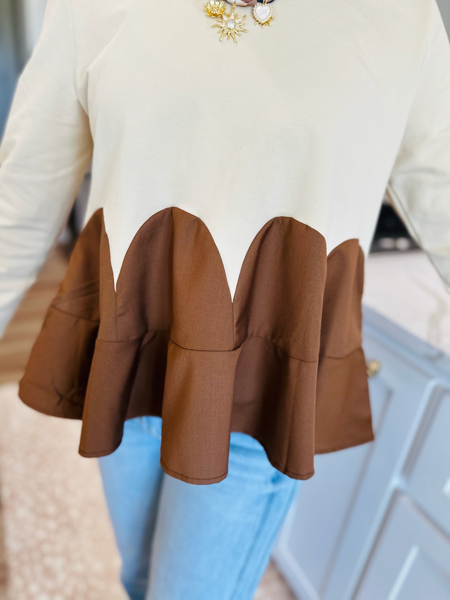 Oatmeal knit top with brown ruffled peplum detail and scalloped hem.