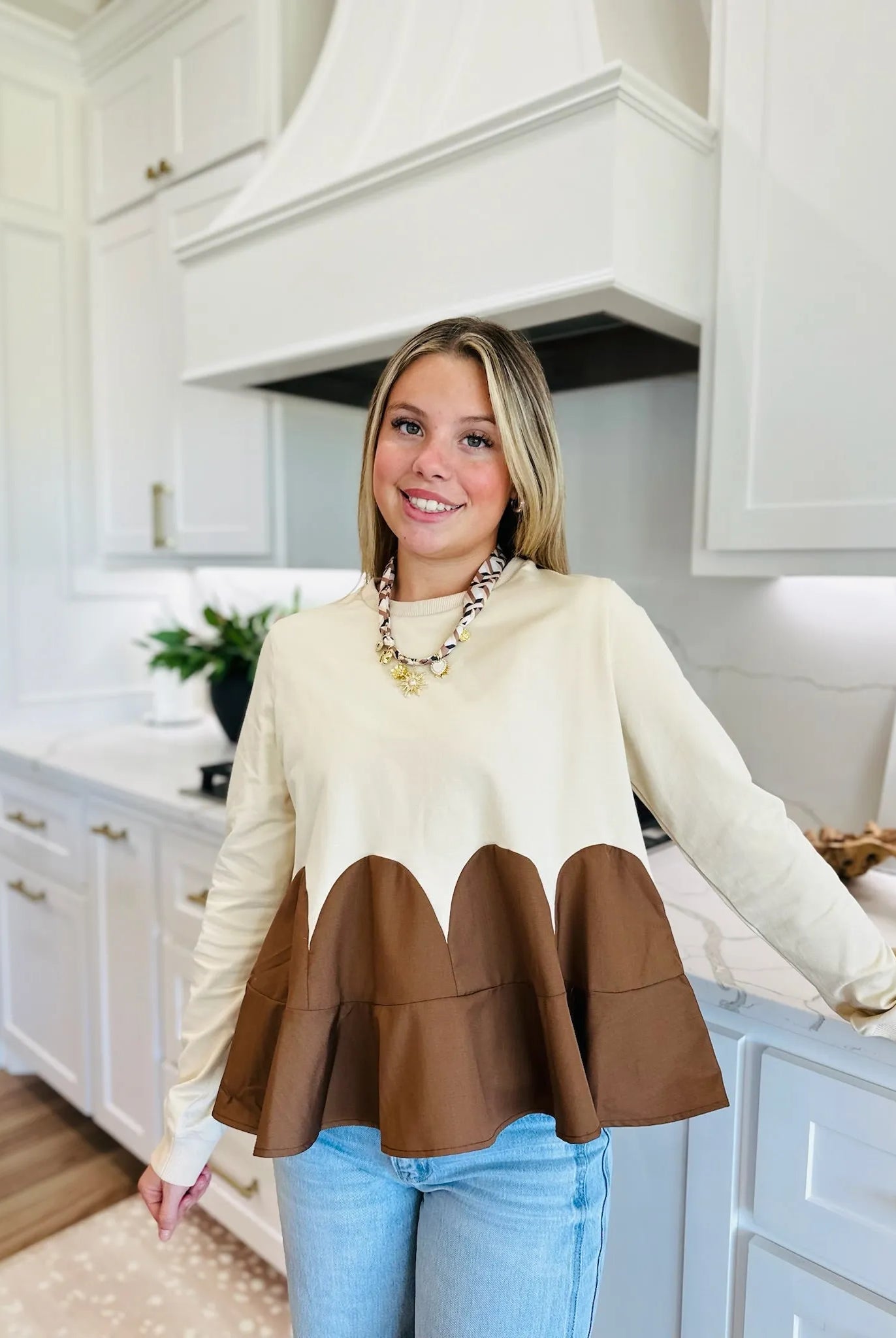 Oatmeal brown mixed media knit top with long sleeves and a scalloped brown hemline. Worn by a young woman.