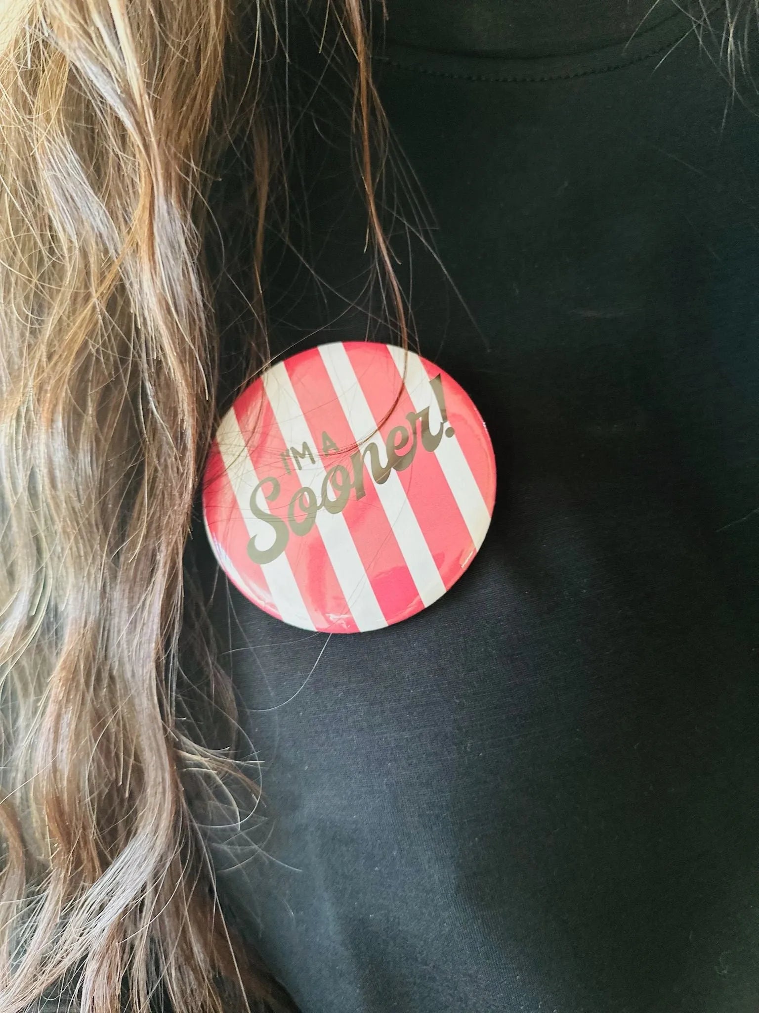 Round Oklahoma Sooner game day button with pink and white stripes and silver text saying "I'm a Sooner!" pinned to a black
