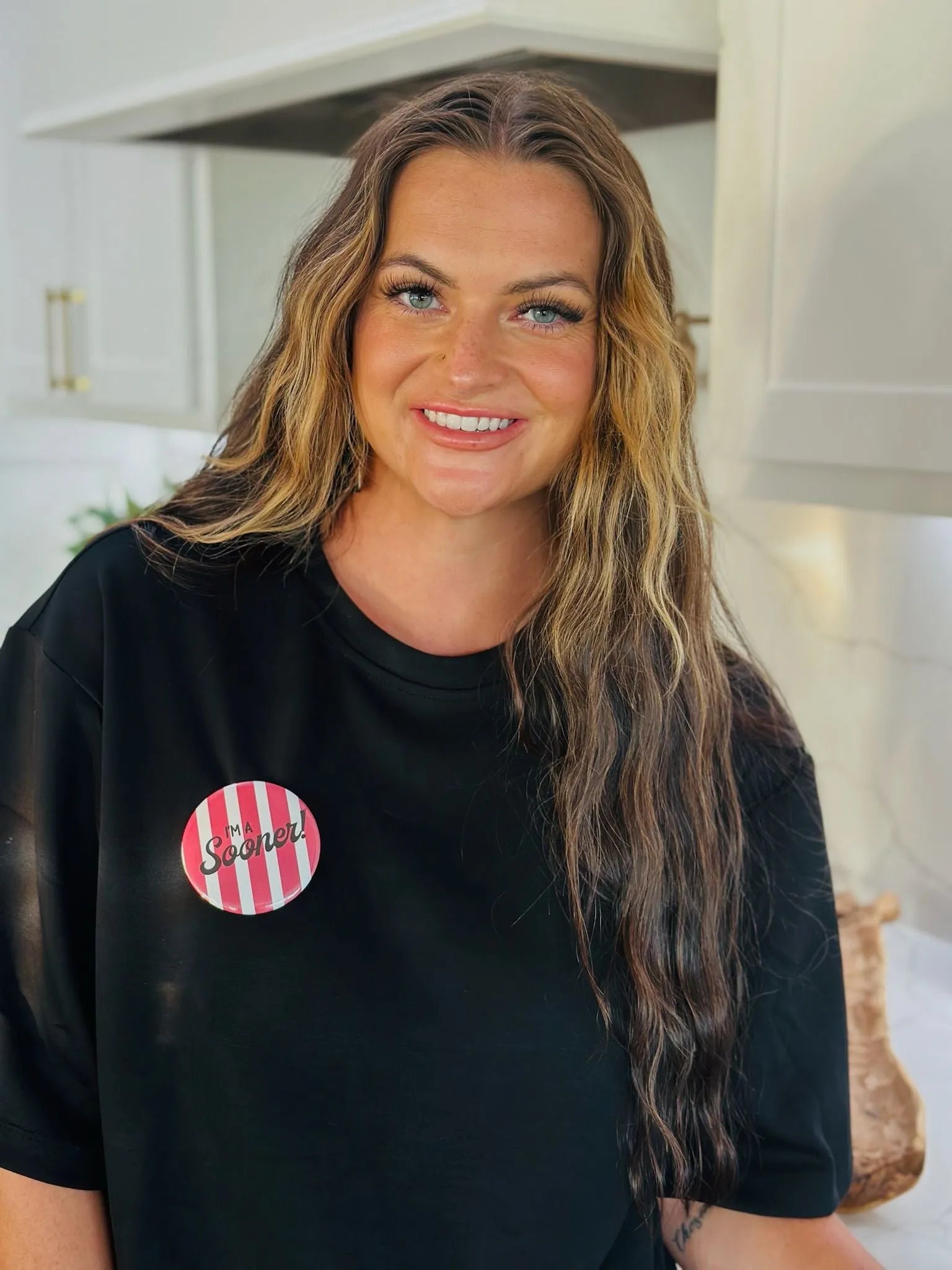 Round pink and white striped button that says "I'M a Sooner!" pinned to a black t-shirt.