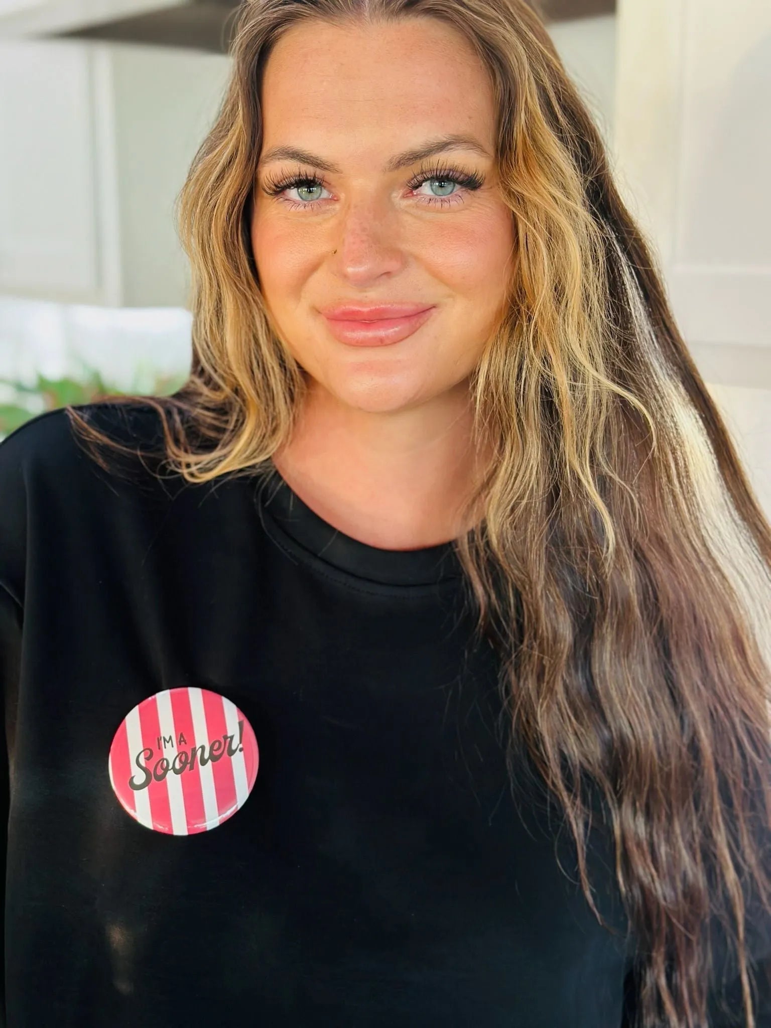 Round button with pink and white stripes and the text "I'M A Sooner!" on a black shirt.
