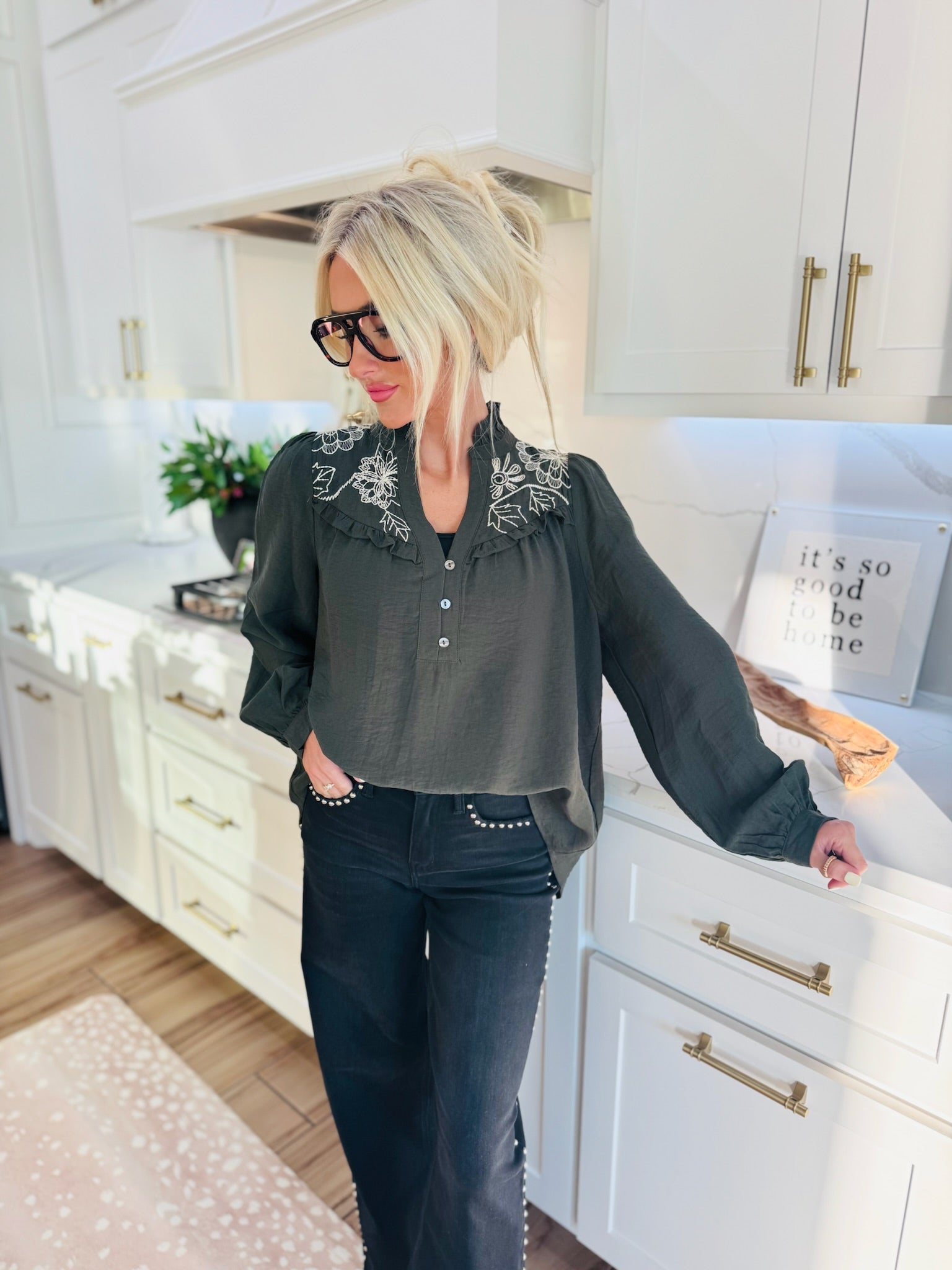 Dark green blouse with white floral embroidery on the collar and front yoke, featuring a ruffled neckline and button