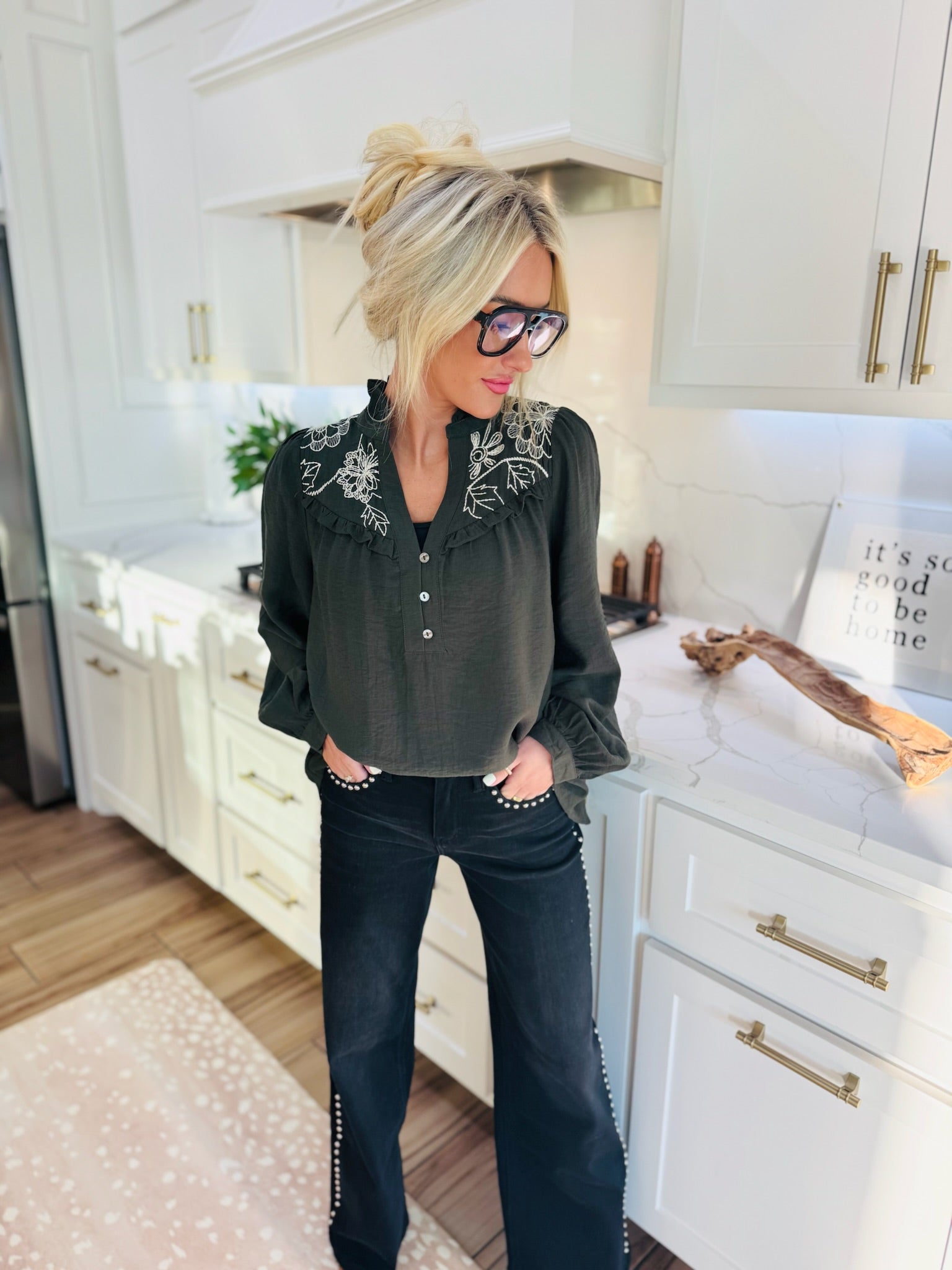 Olive floral embroidered blouse with ruffled collar and button placket, paired with black embellished flare jeans.