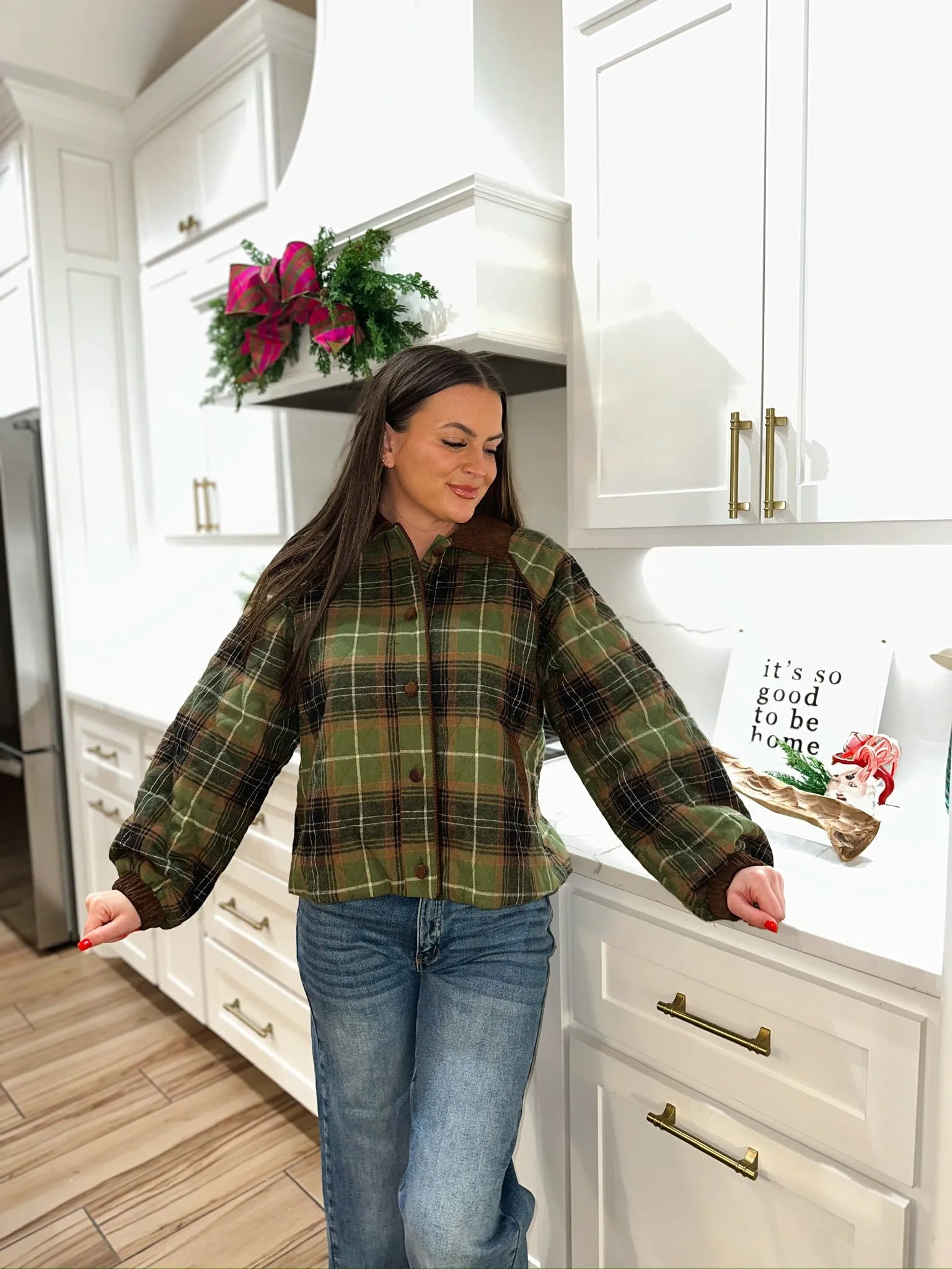 Woman in olive green quilted plaid puffer jacket with brown collar and cuffs, paired with blue jeans.