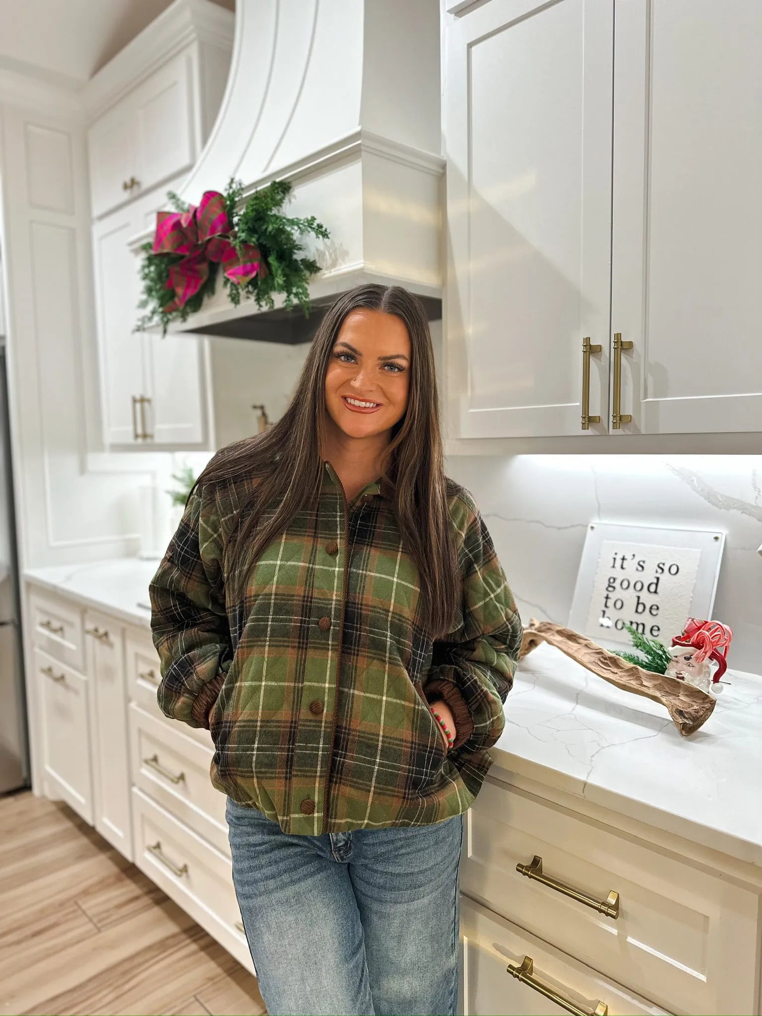 Woman wearing a green quilted plaid puffer jacket with brown accents and blue jeans.
