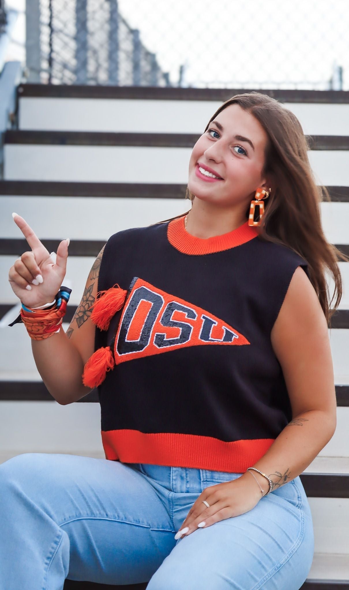 Orange and white checkered statement earrings with orange tassels, worn by a woman with a dark blue and orange OSU pennant