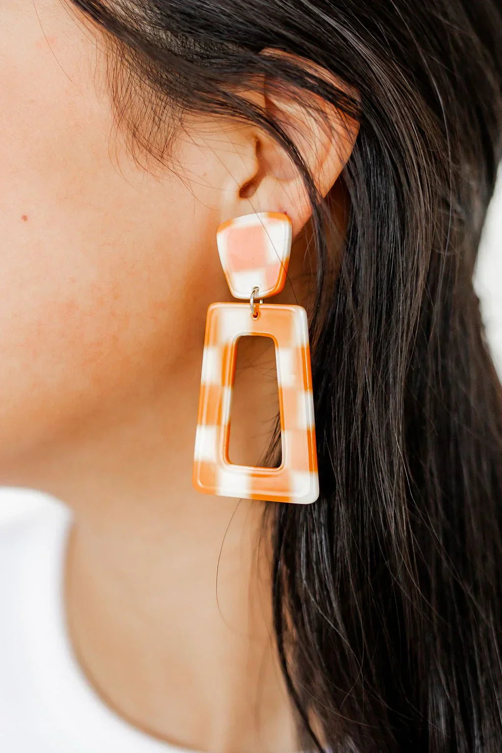 Orange and white checkered statement earrings with a rounded top and a rectangular hollow center.