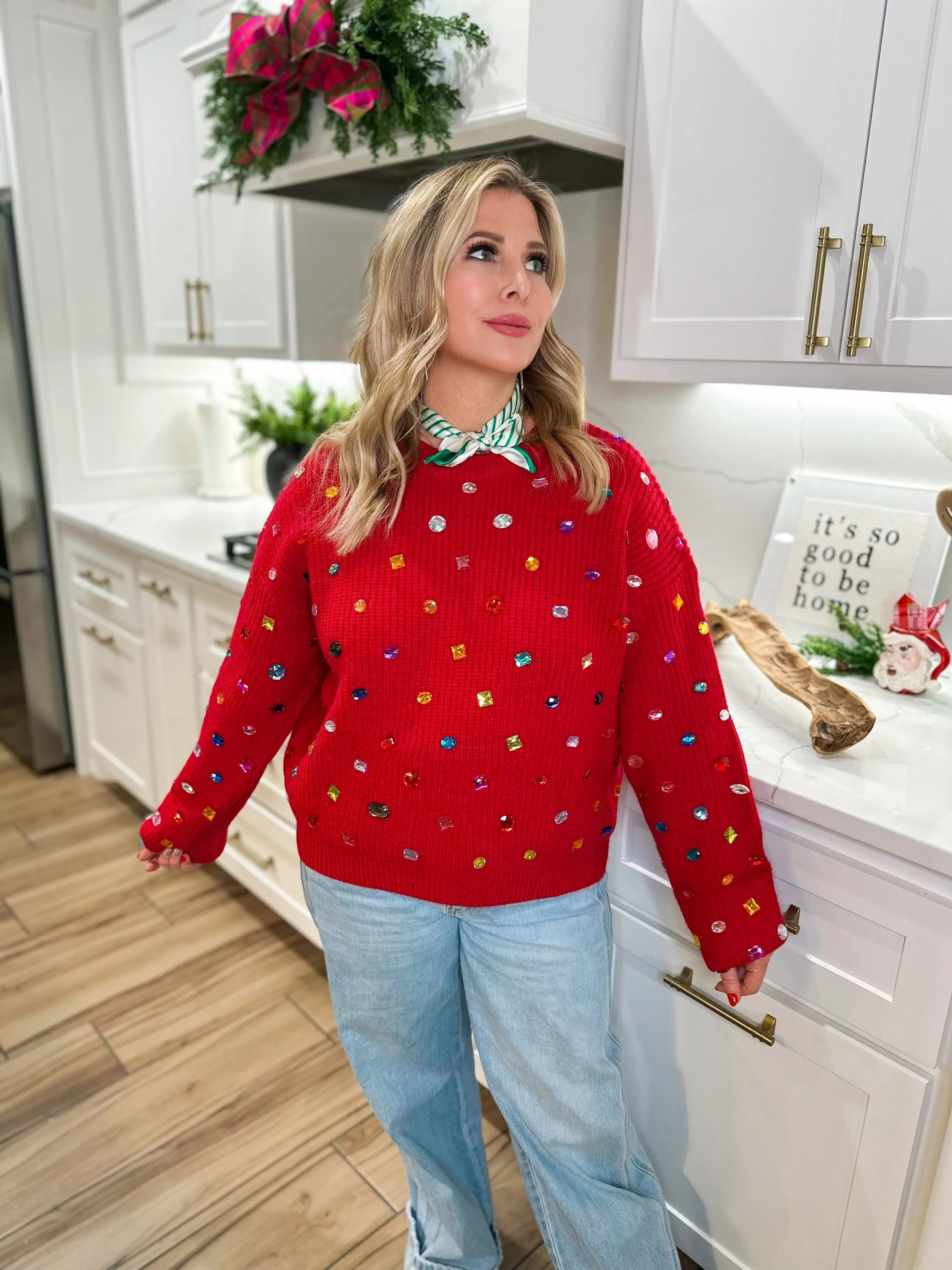 Red oversized sweater adorned with colorful jeweled embellishments and a green and white striped scarf.