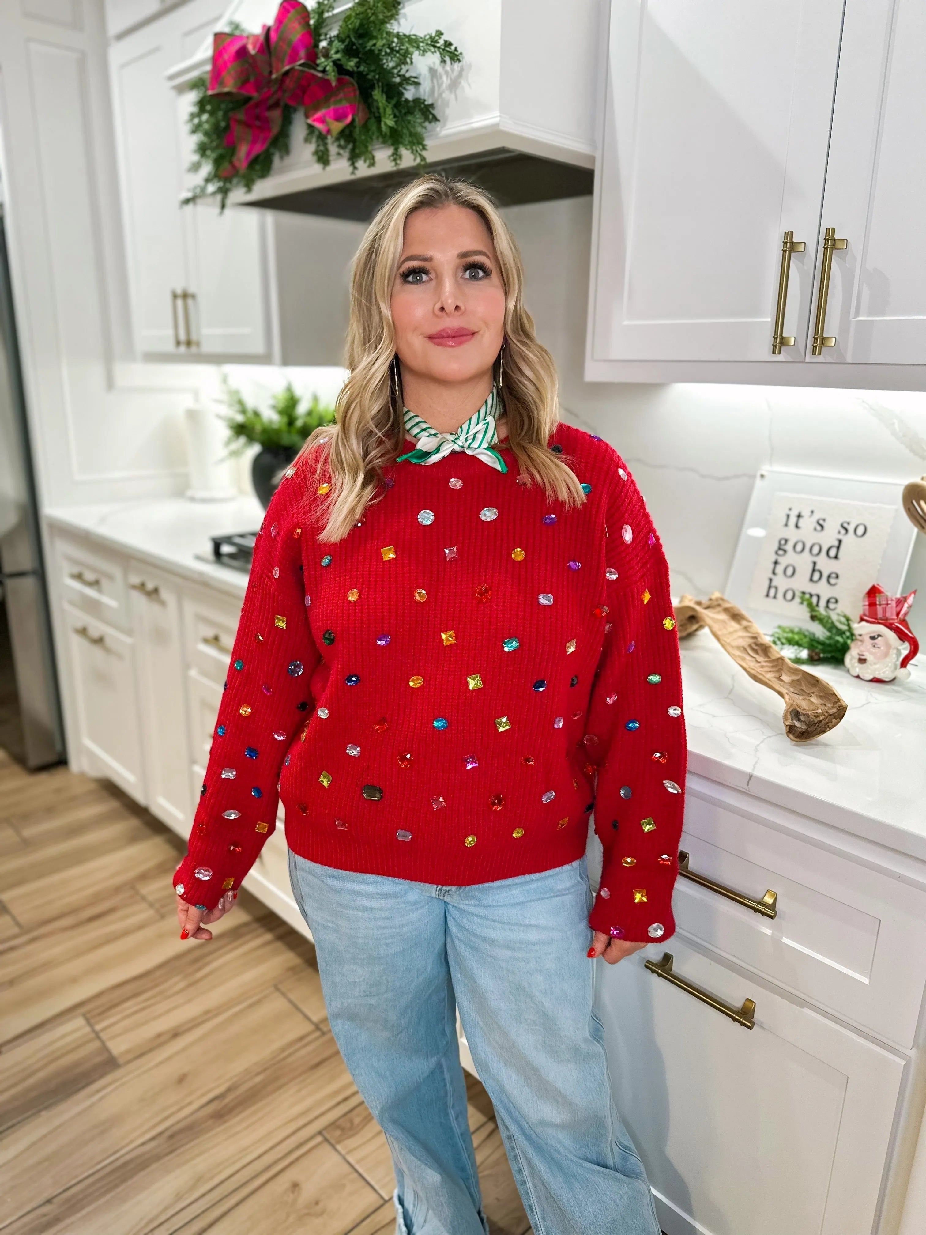 Red oversized sweater with colorful scattered rhinestones and gems. Long sleeves, crew neck, paired with light wash jeans