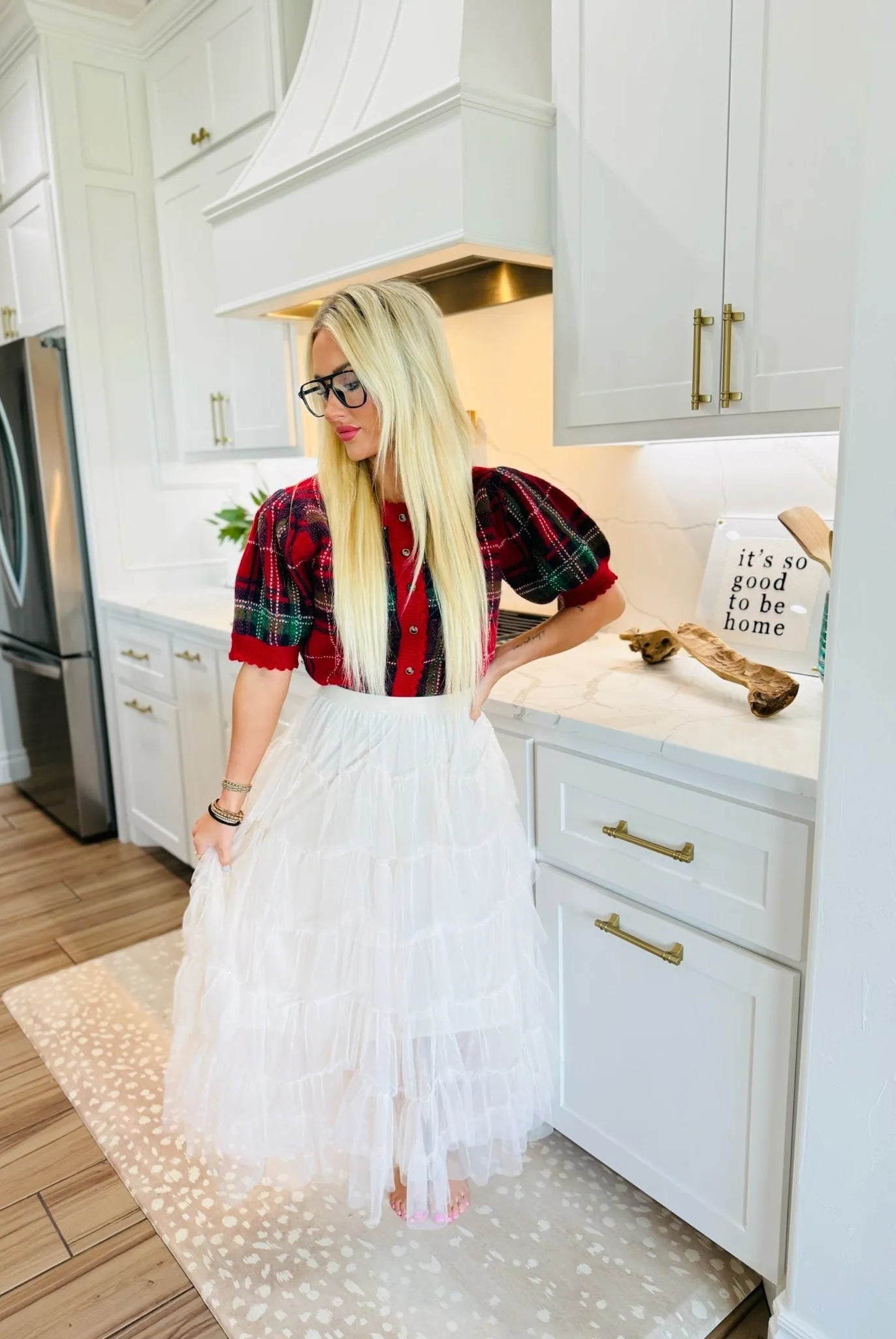 A blonde woman wears a white tiered ruffle mesh midi skirt and a red and green plaid puff-sleeve top. She stands in a