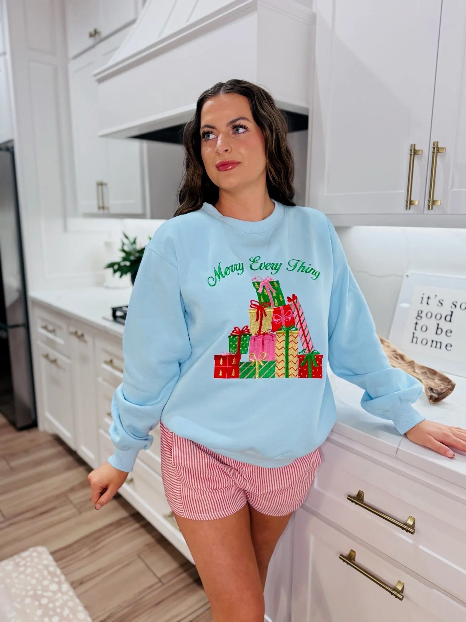 Light blue crewneck sweatshirt with "Merry Everything" text and a stacked pile of colorful Christmas presents embroidered