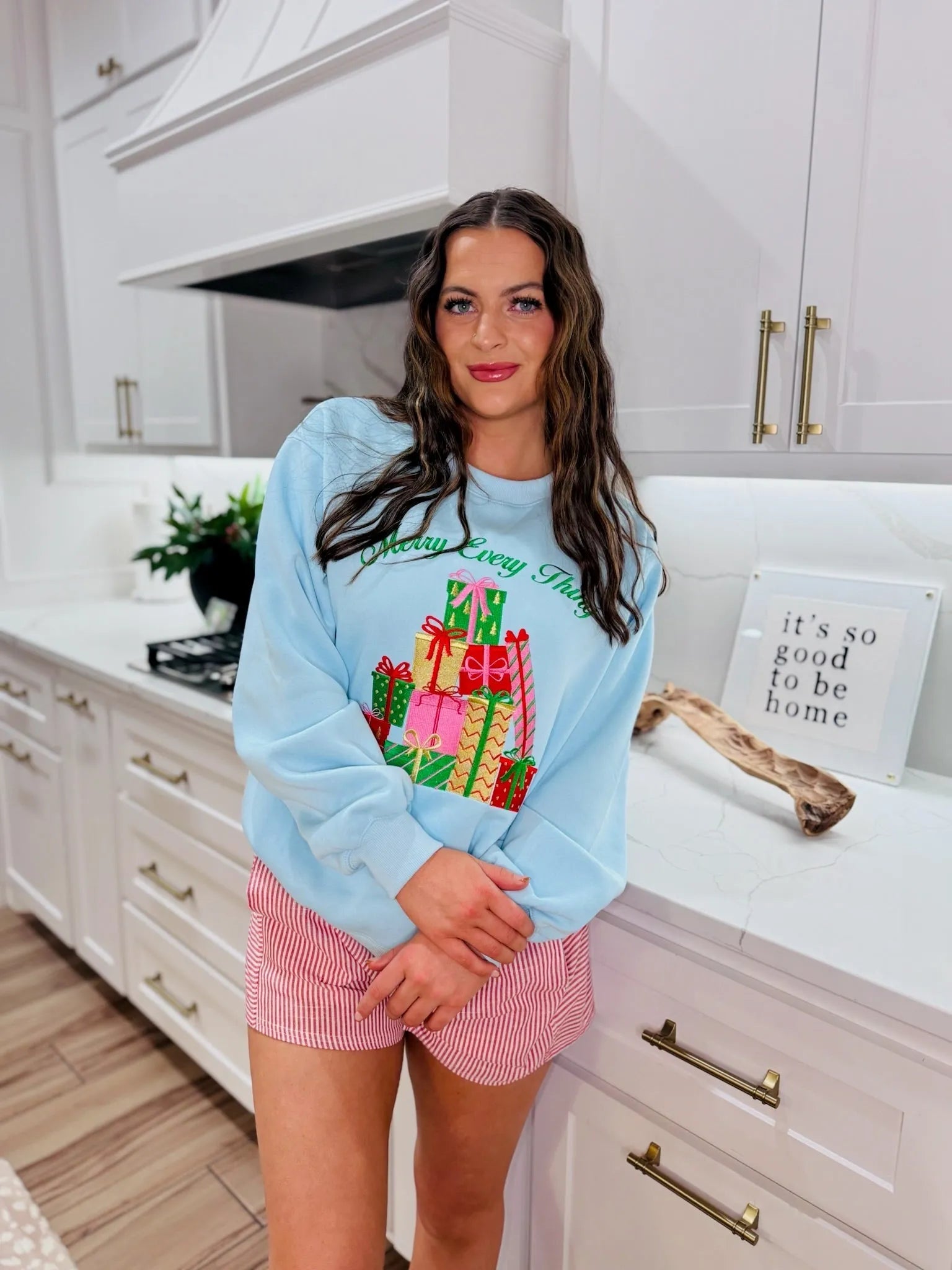 Light blue sweatshirt with a pile of colorful Christmas presents graphic and text 'Merry Everything'. Features a woman