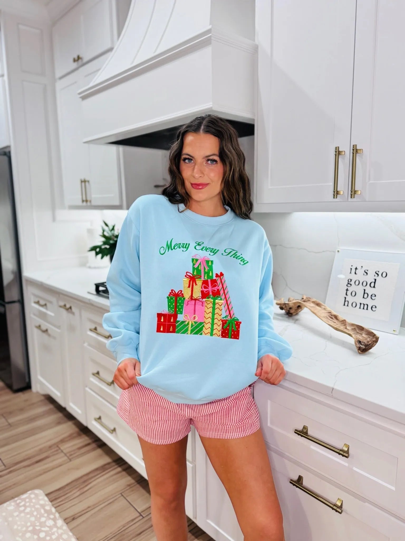 Light blue sweatshirt with 'Merry Every Thing' text and a pile of colorful Christmas gifts. Features red, green, and pink