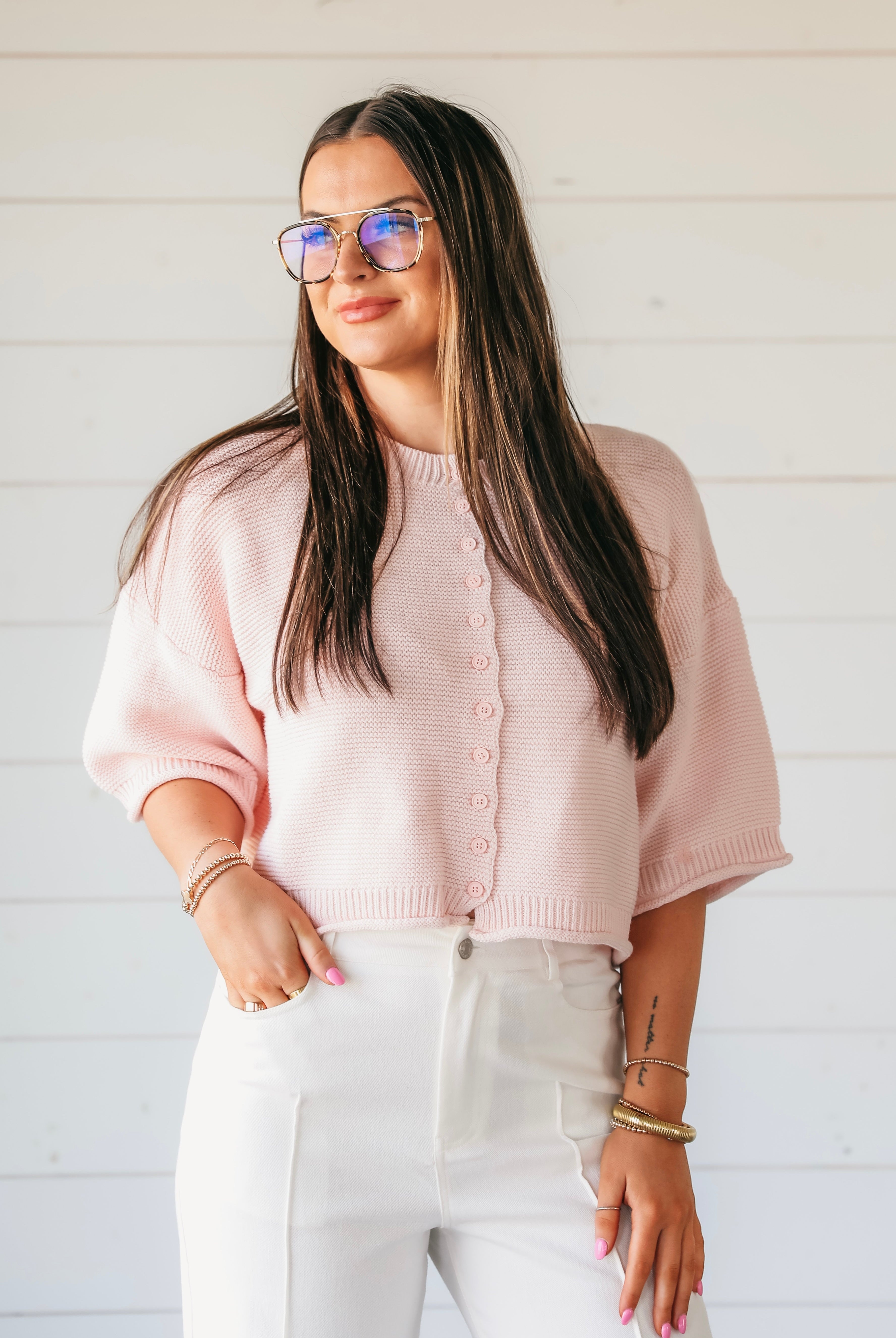 Woman wearing a light pink waffle knit button-down cardigan sweater with short sleeves and white pants. white pants.