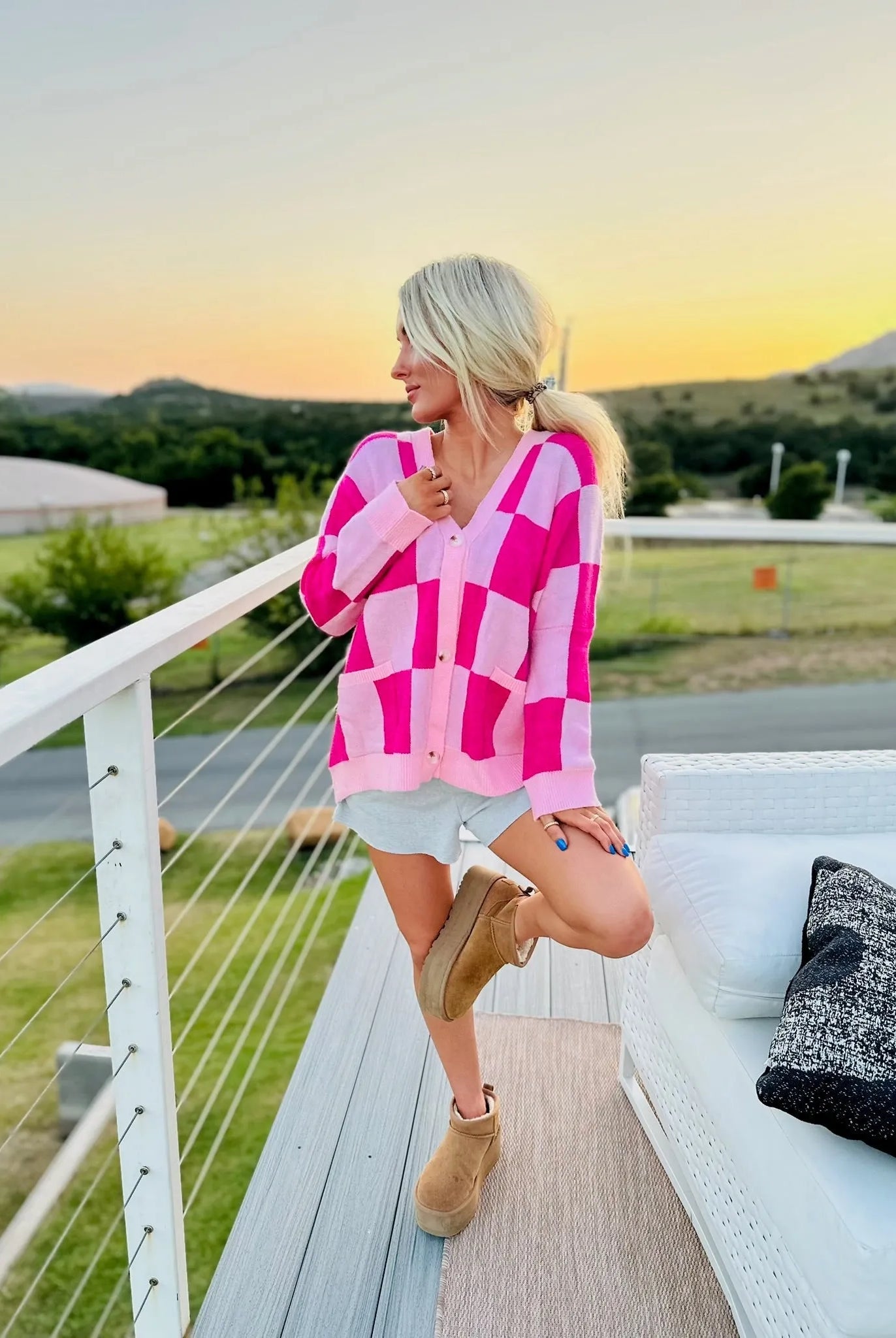 Woman wearing a pink and hot pink checkered oversized cardigan with a V-neck and buttons, paired with grey shorts and brown