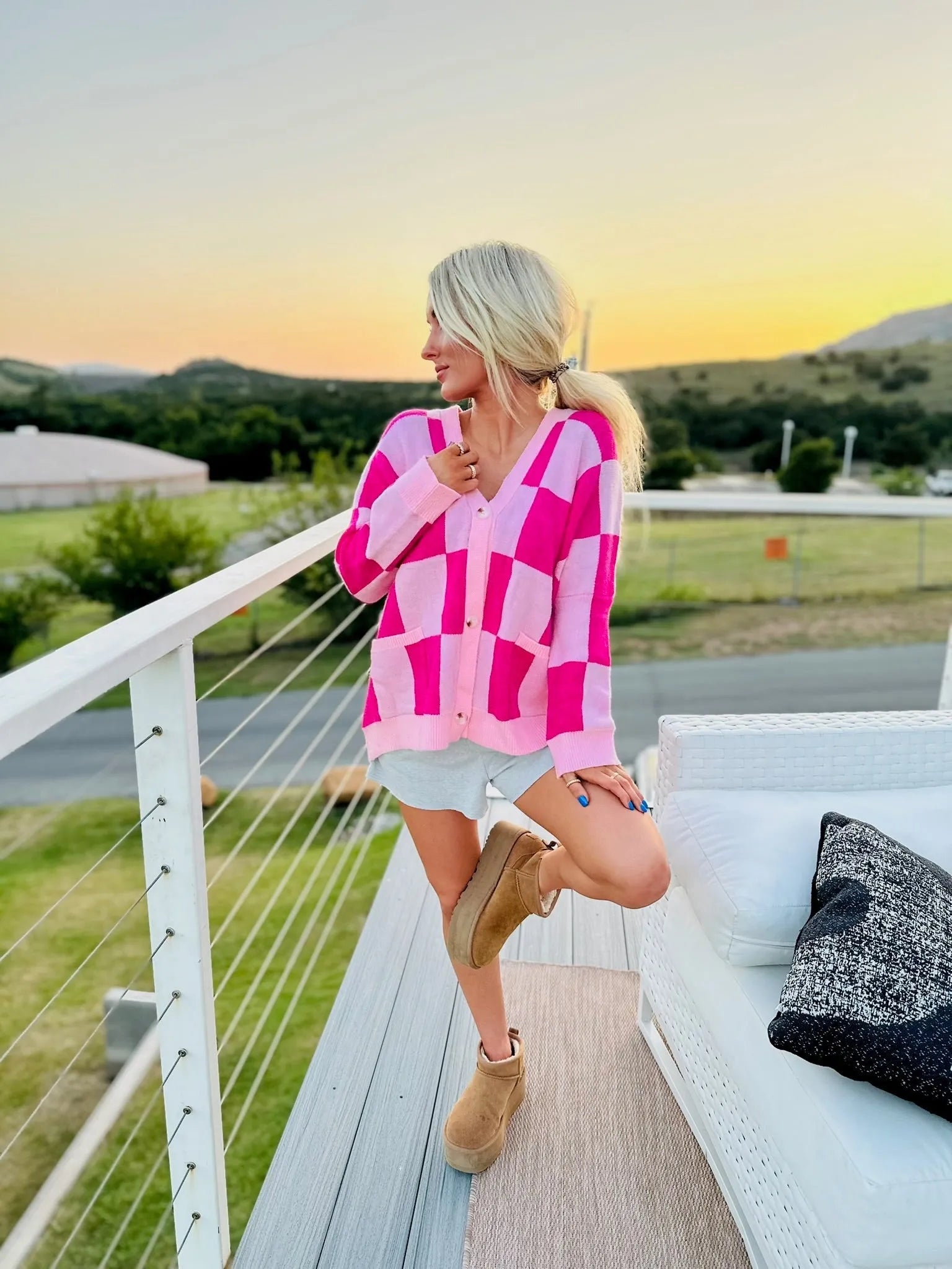 Woman wearing a pink and hot pink checkered oversized cardigan with a V-neck and buttons, paired with grey shorts and brown