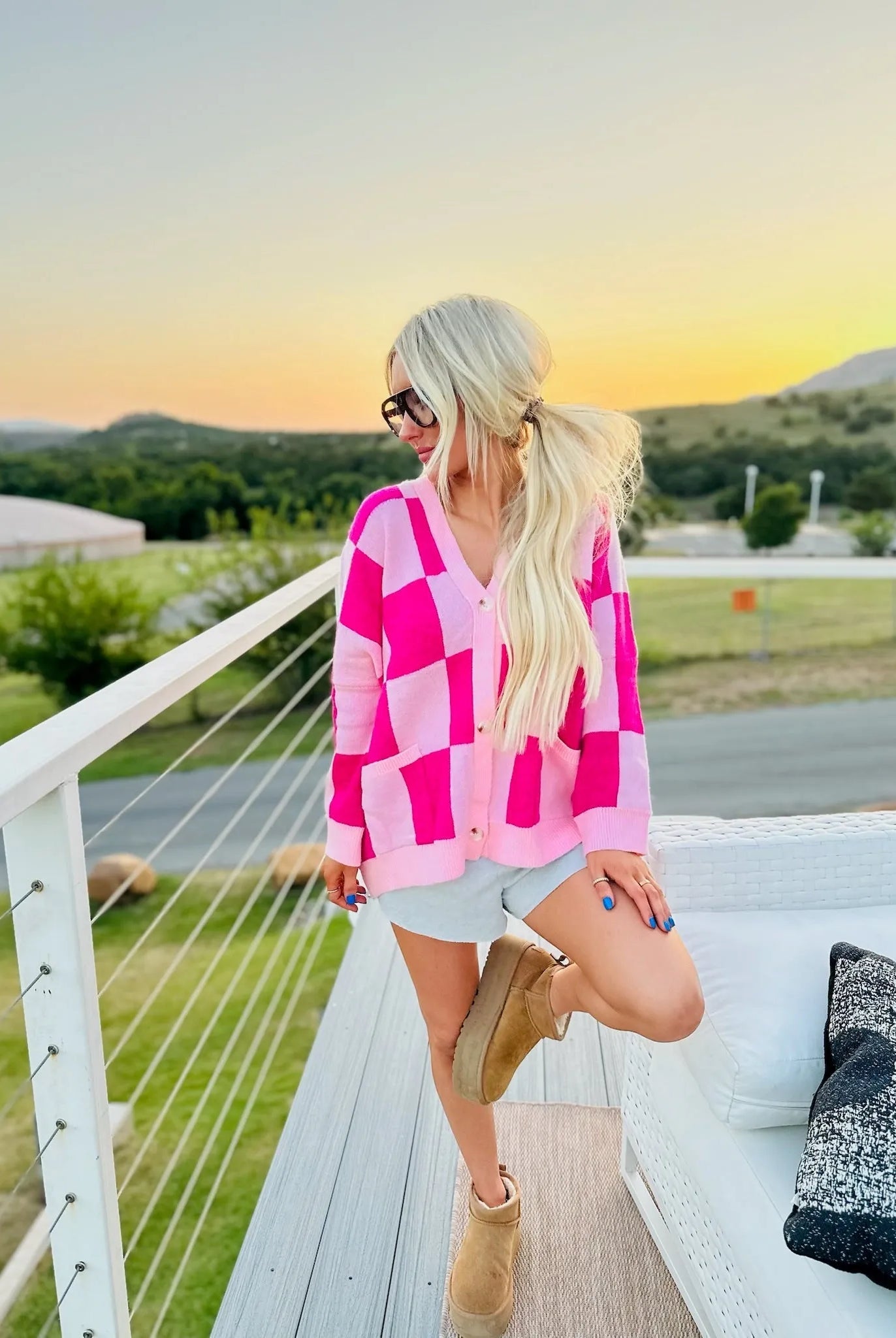 Pink checkered long-sleeve cardigan with v-neck and button closure, worn by a woman outdoors at sunset.