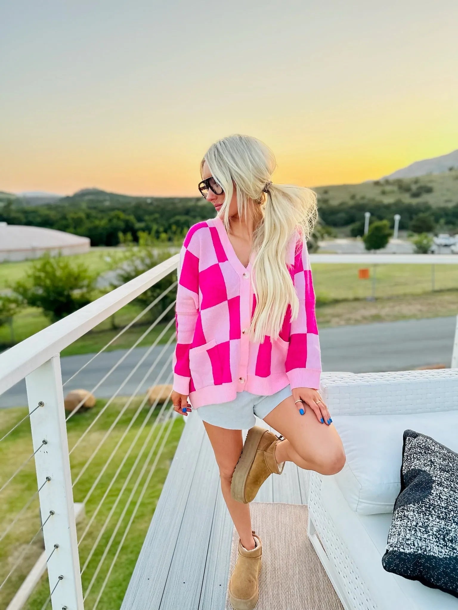 Pink checkered long-sleeve cardigan with v-neck and button closure, worn by a woman outdoors at sunset.