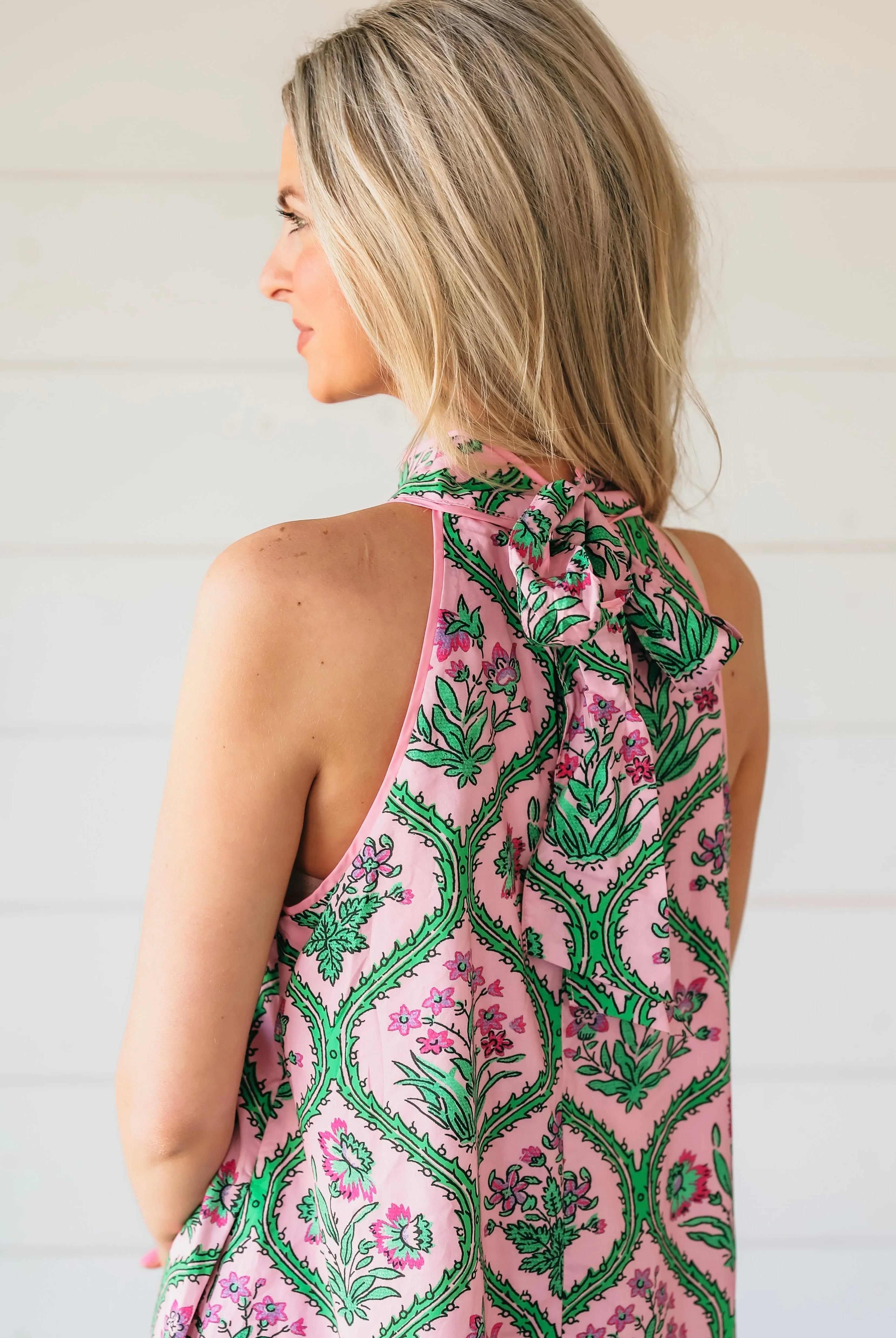 Pink floral halter mini dress with green vine pattern and bow tie at the back.