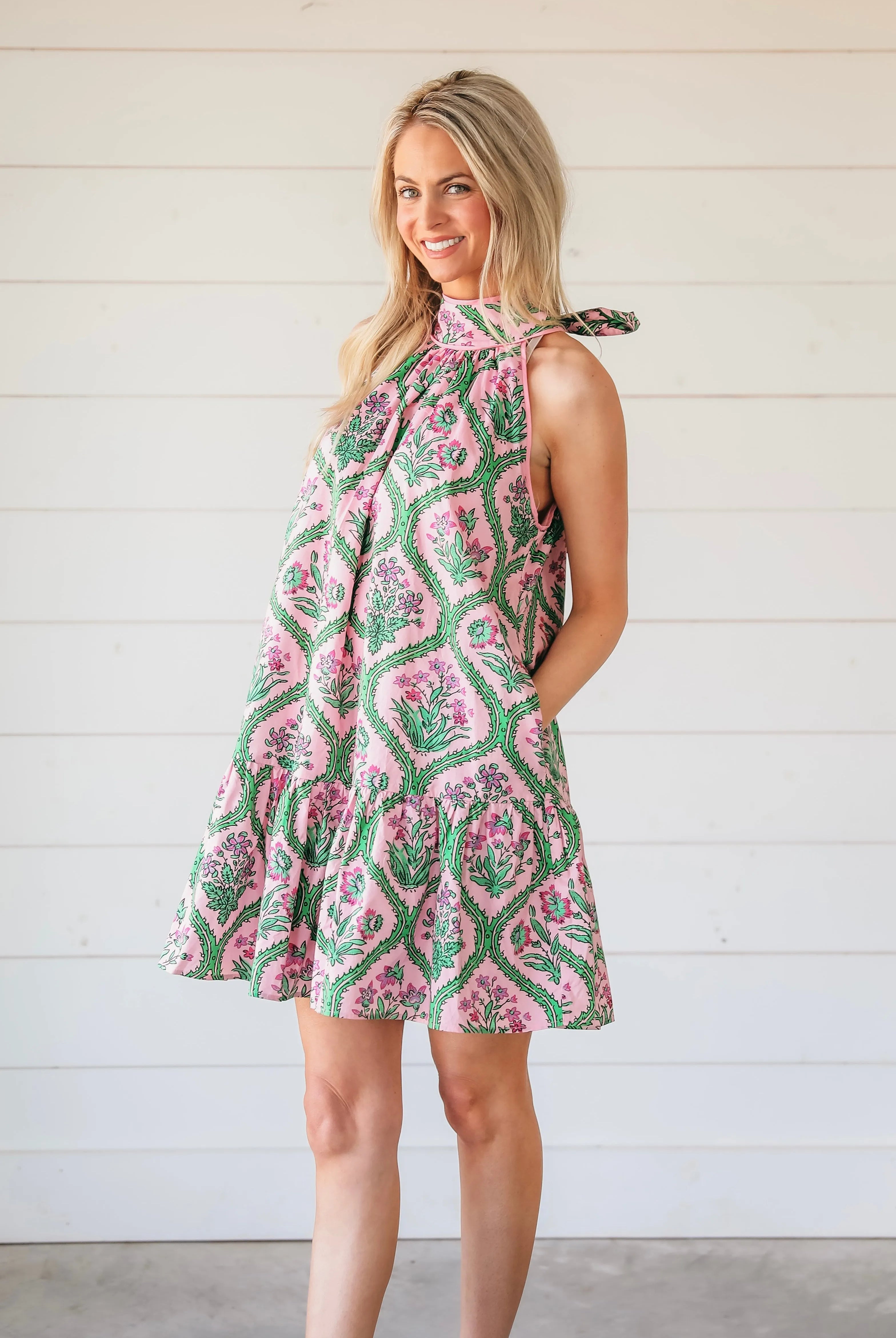 Pink floral halter mini dress with a tie detail at the shoulder. The dress features a repeating pattern of pink flowers and