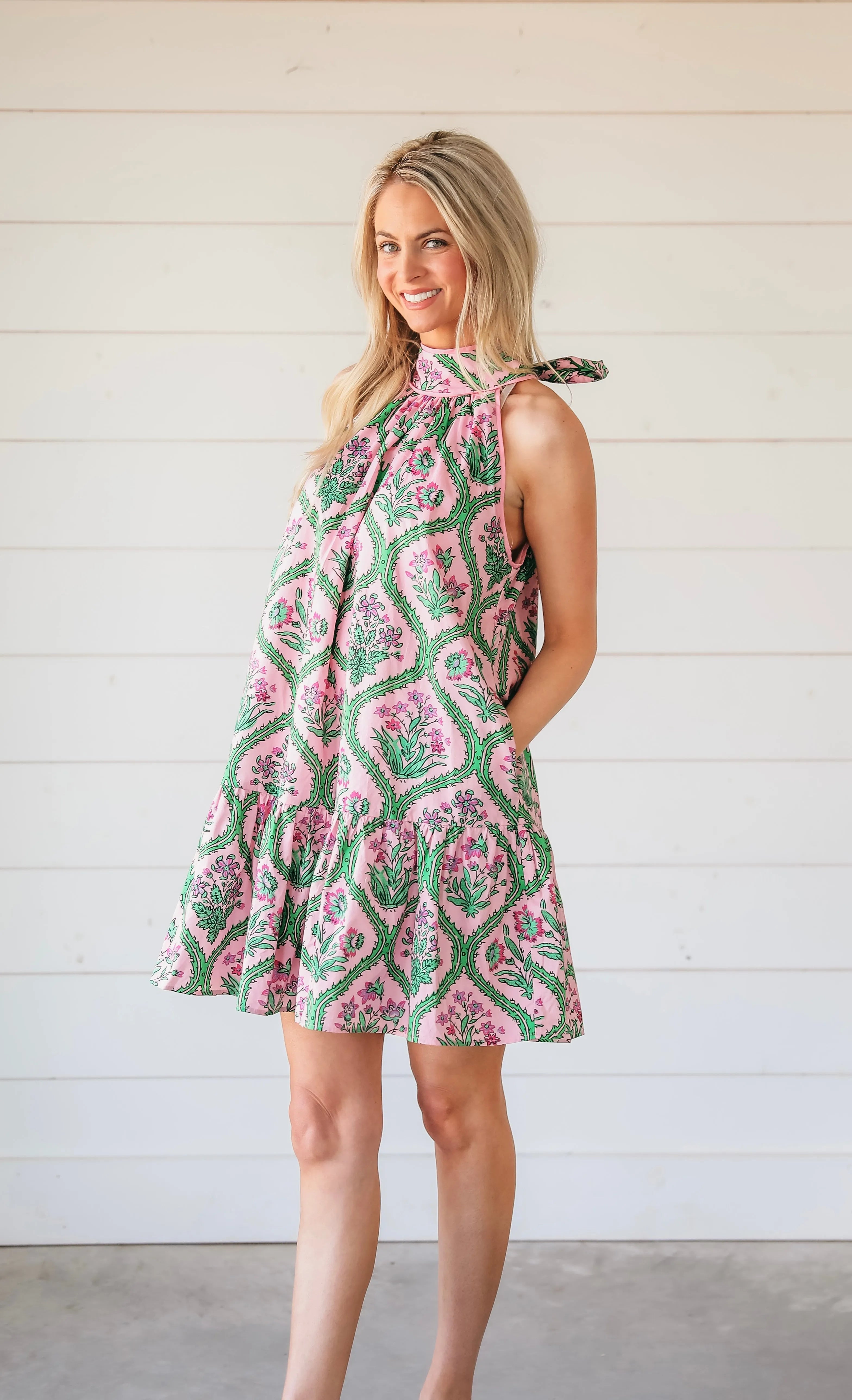 Pink floral halter mini dress with a tie detail at the shoulder. The dress features a repeating pattern of pink flowers and