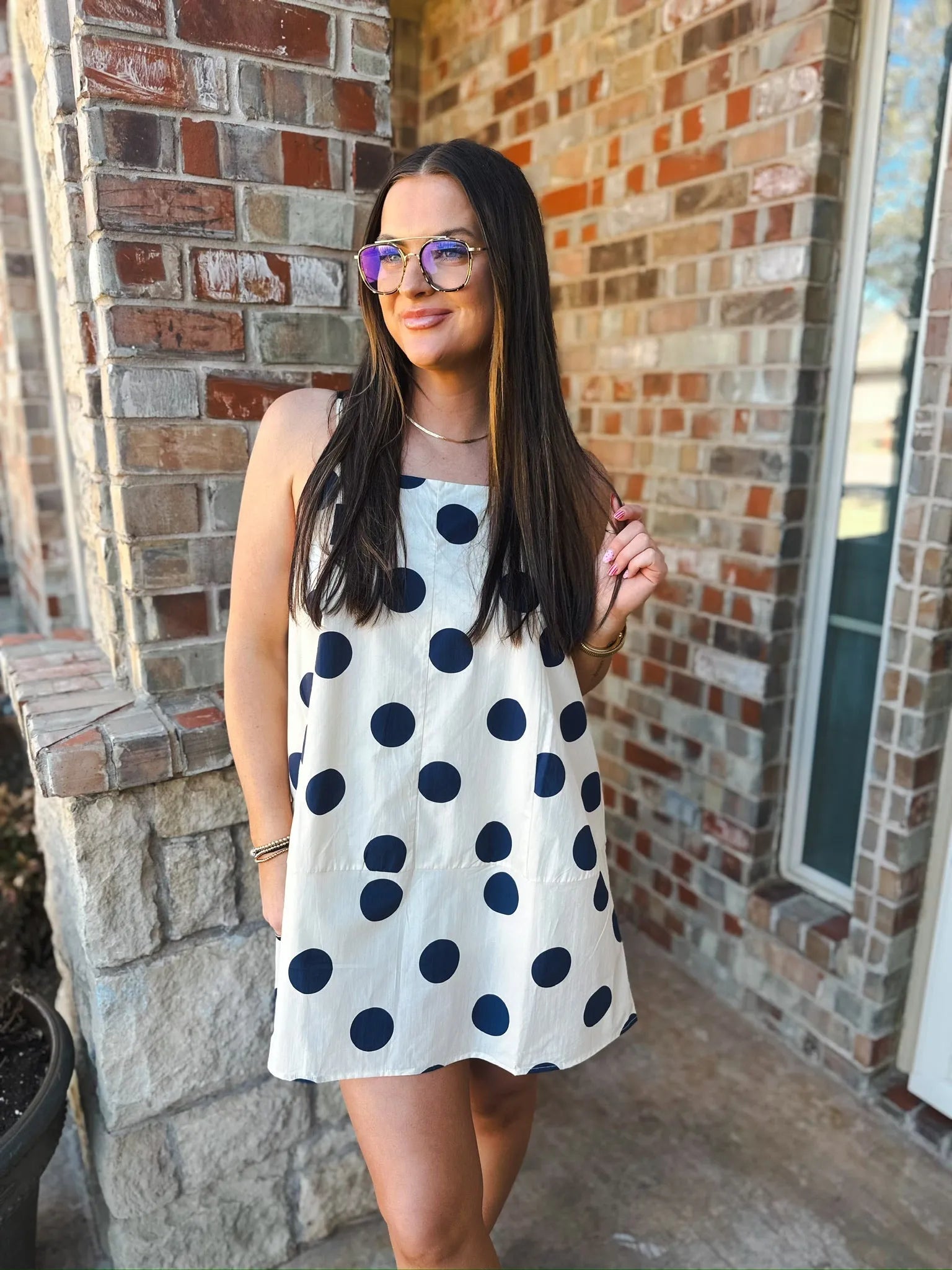 Woman wearing a cream mini dress with navy polka dots, spaghetti straps, and glasses.