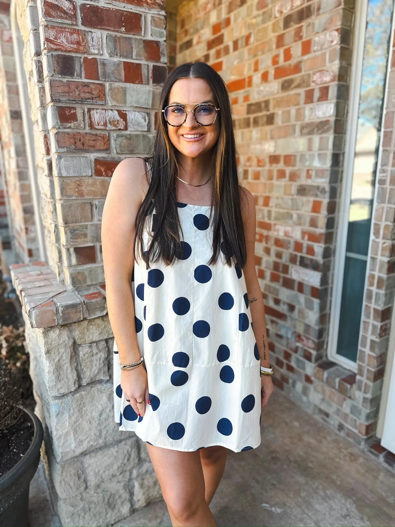 Woman wearing a cream mini dress with navy polka dots, square neckline, and back straps.