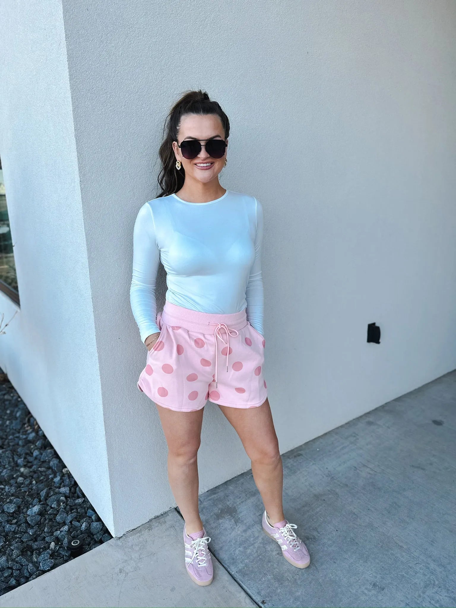 Poppy & Pine blush pink polka dot shorts with drawstring waist, worn by a woman with sunglasses and a white long-sleeve