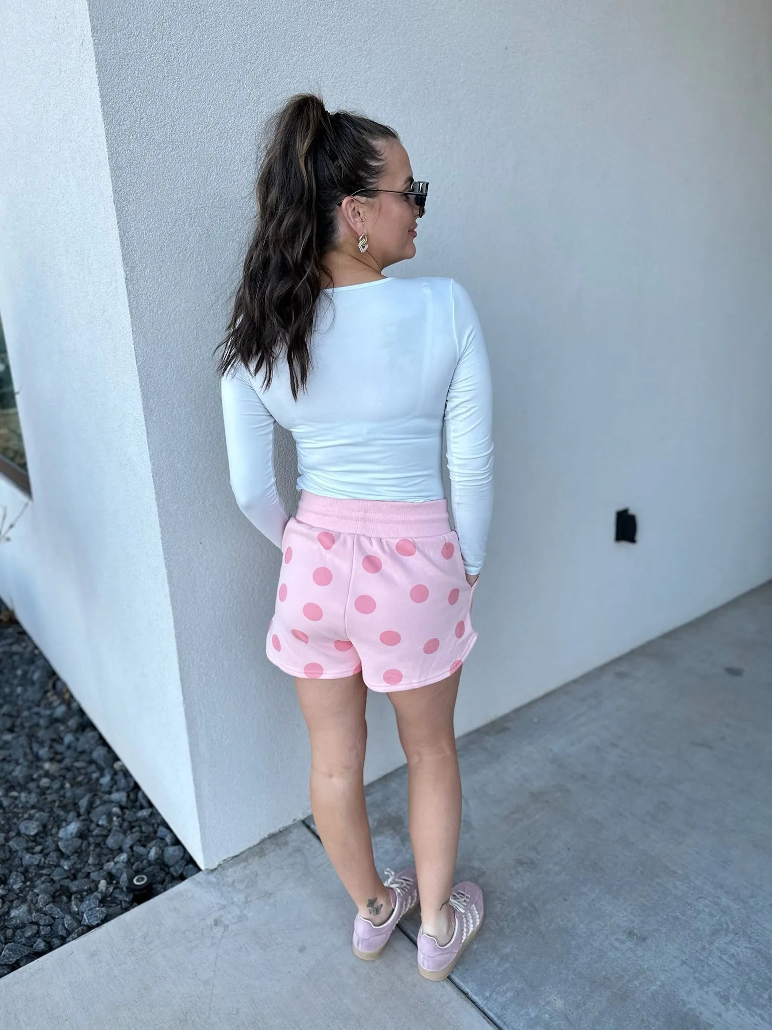 Poppy & Pine blush pink polka dot shorts worn by a woman with a white long-sleeve top.