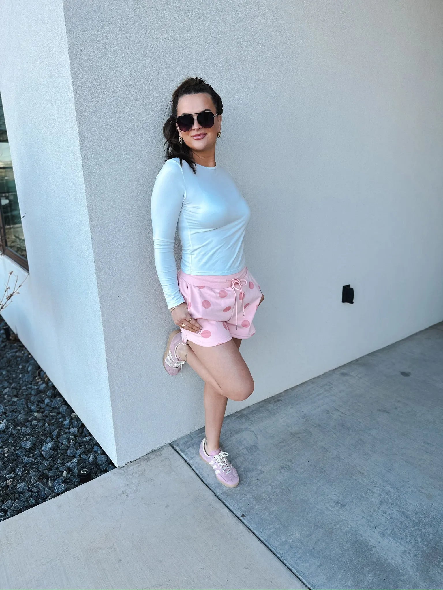 Poppy & Pine blush pink polka dot shorts with drawstring waist, paired with a white long-sleeve shirt and pink sneakers.