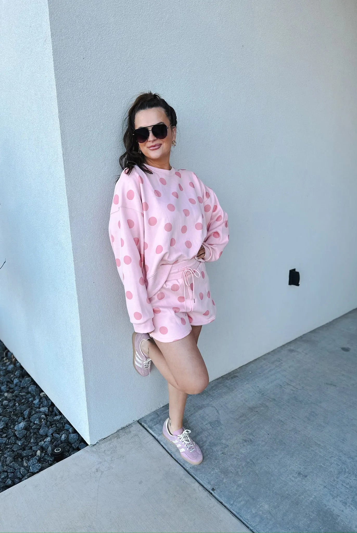 Poppy & Pine blush pink polka dot sweatshirt and matching shorts set. Model wears sunglasses and pink sneakers, leaning