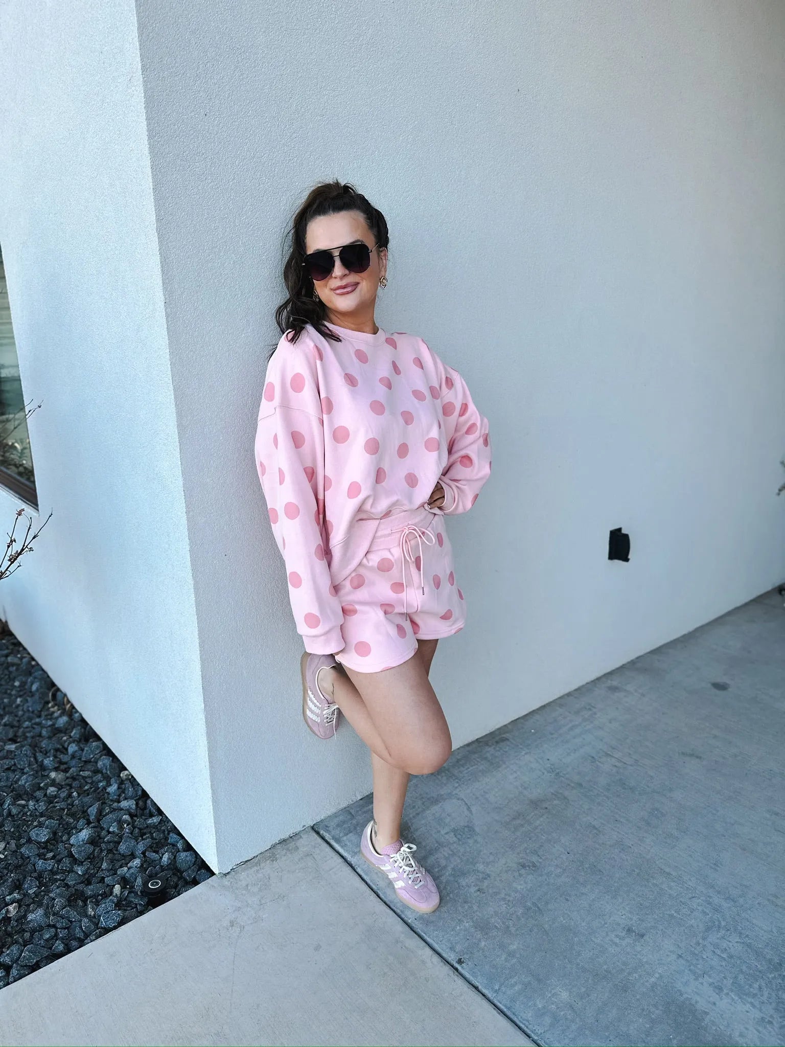Poppy & Pine blush pink polka dot sweatshirt and matching shorts set. Model wears sunglasses and pink sneakers, leaning