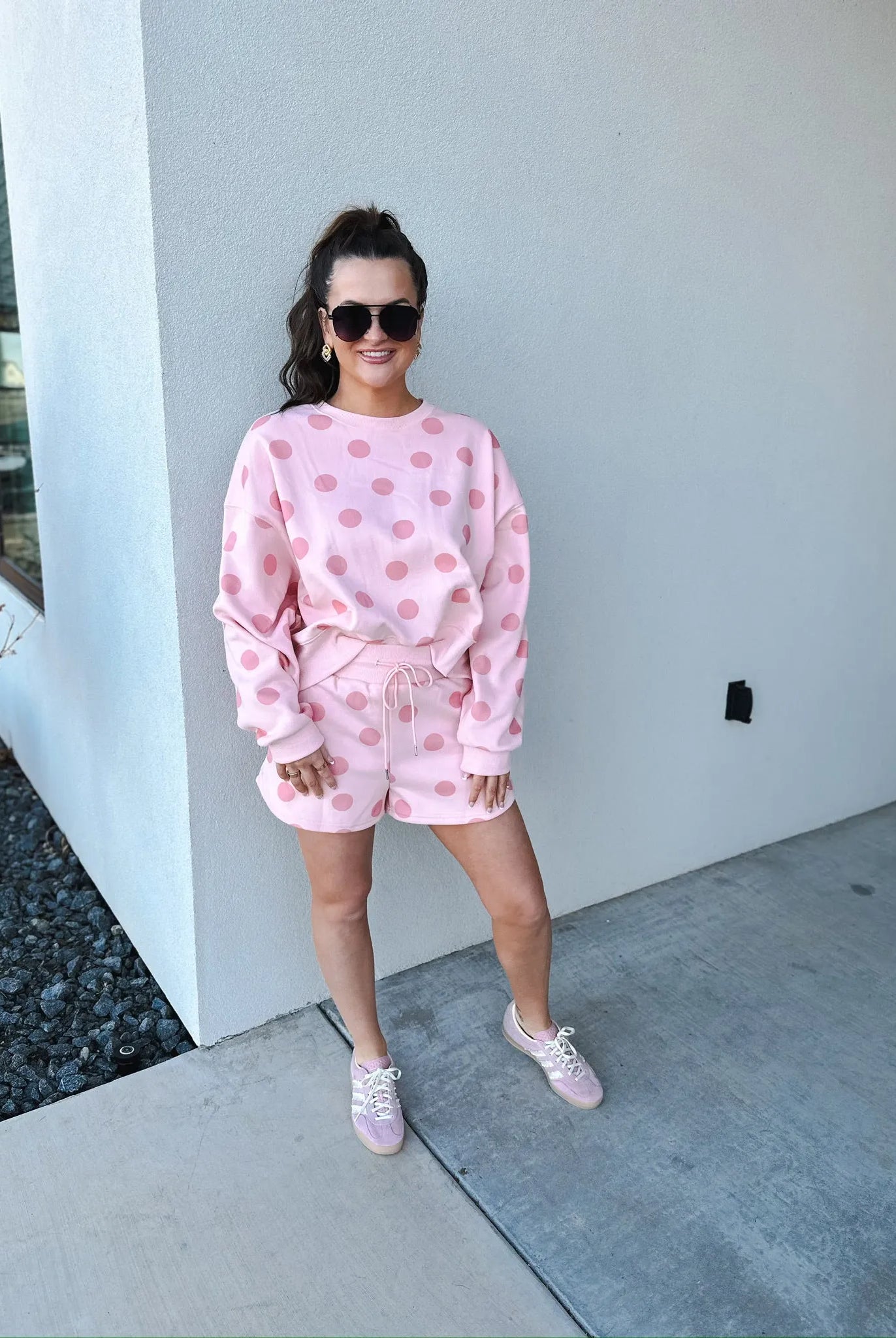 Poppy & Pine blush pink polka dot sweatshirt and matching shorts set on a woman wearing sunglasses and pink sneakers.