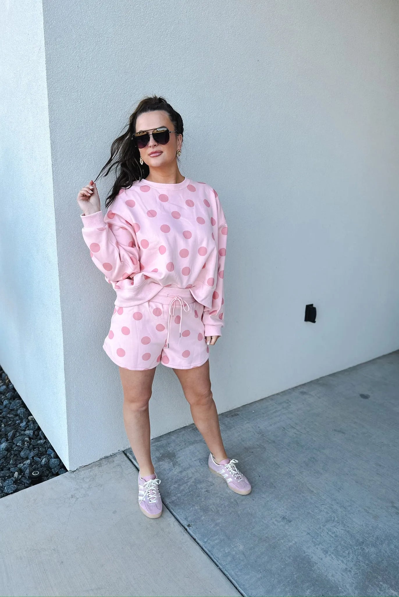 Poppy & Pine blush pink polka dot sweatshirt and matching shorts set. Woman wearing sunglasses, gold earrings, pink sneakers.