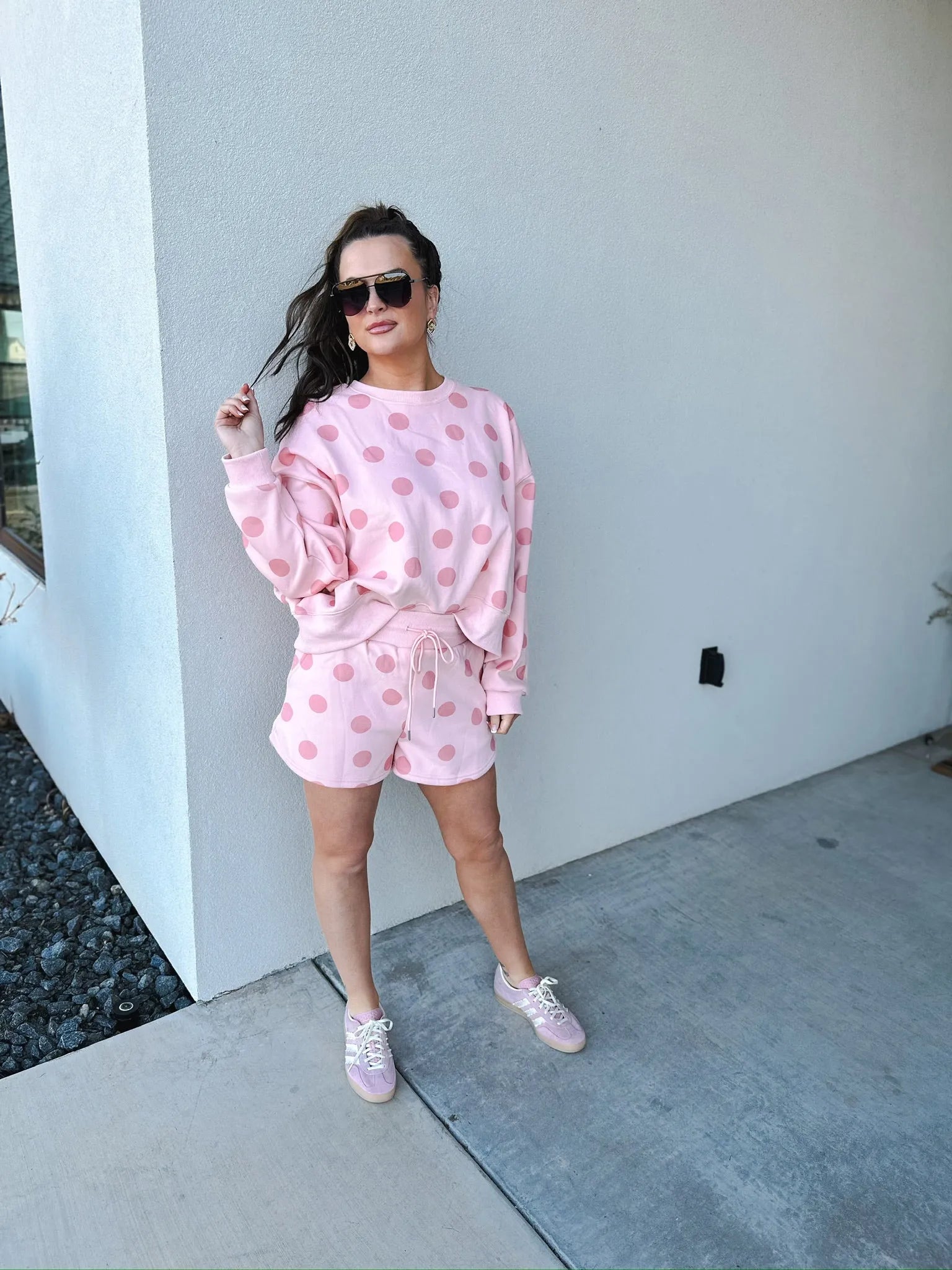 Poppy & Pine blush pink polka dot sweatshirt and matching shorts set. Woman wearing sunglasses, gold earrings, pink sneakers.