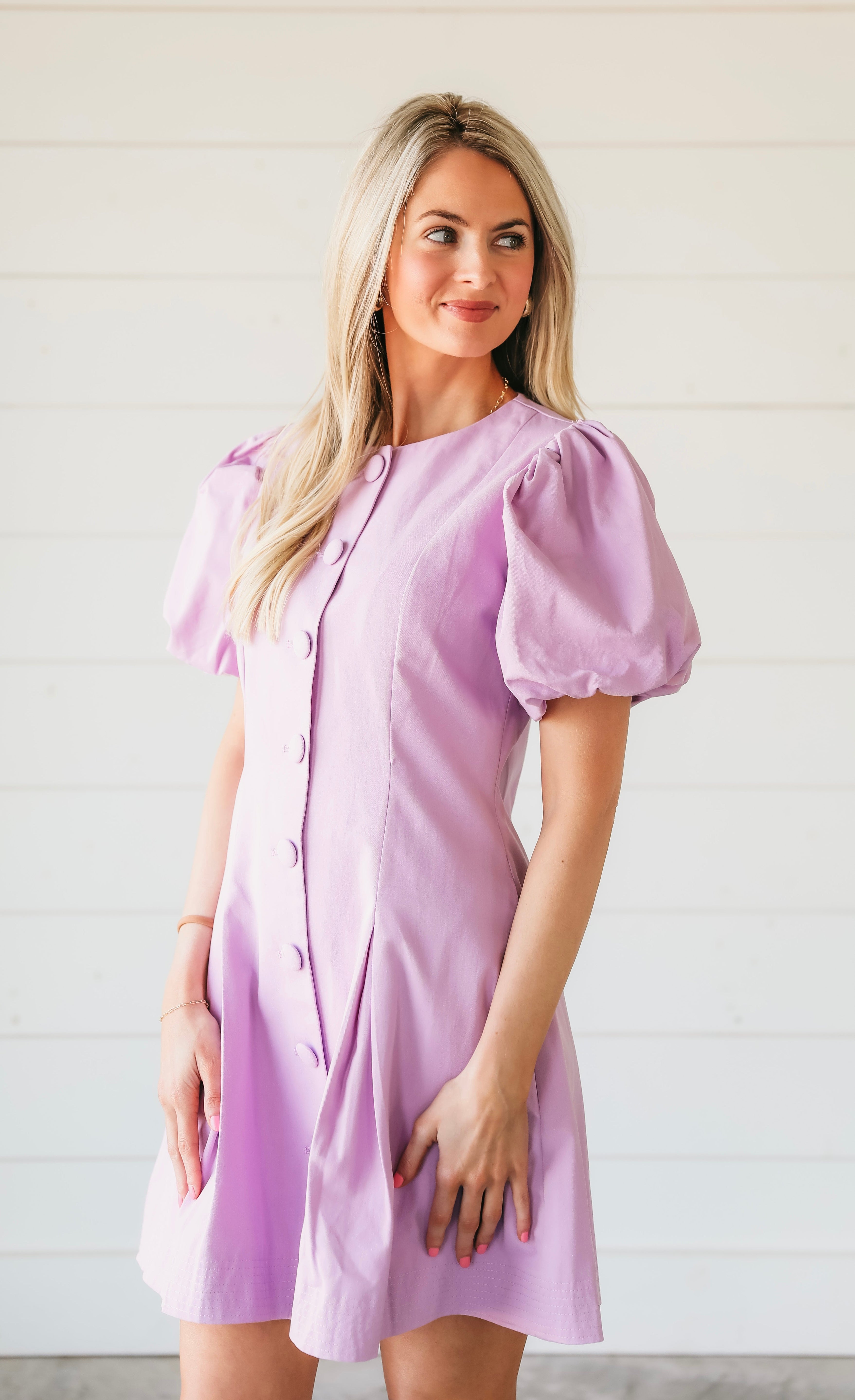 Woman wearing a structured purple mini dress with puff sleeves and a button-down front.
