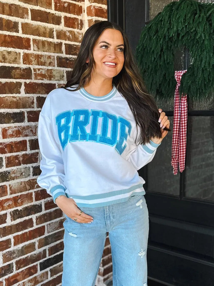 White Queen Of Sparkles Bride sweatshirt with blue athletic lettering and trim, light blue striped cuffs and neckline, worn