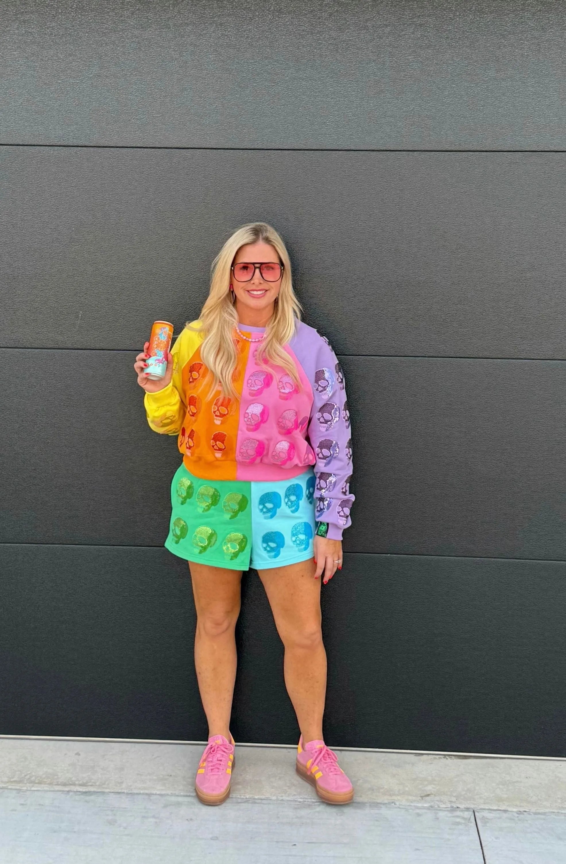 Woman wearing multi-colored shorts with all-over skull print. Shorts are color-blocked green, aqua, pink, and purple with