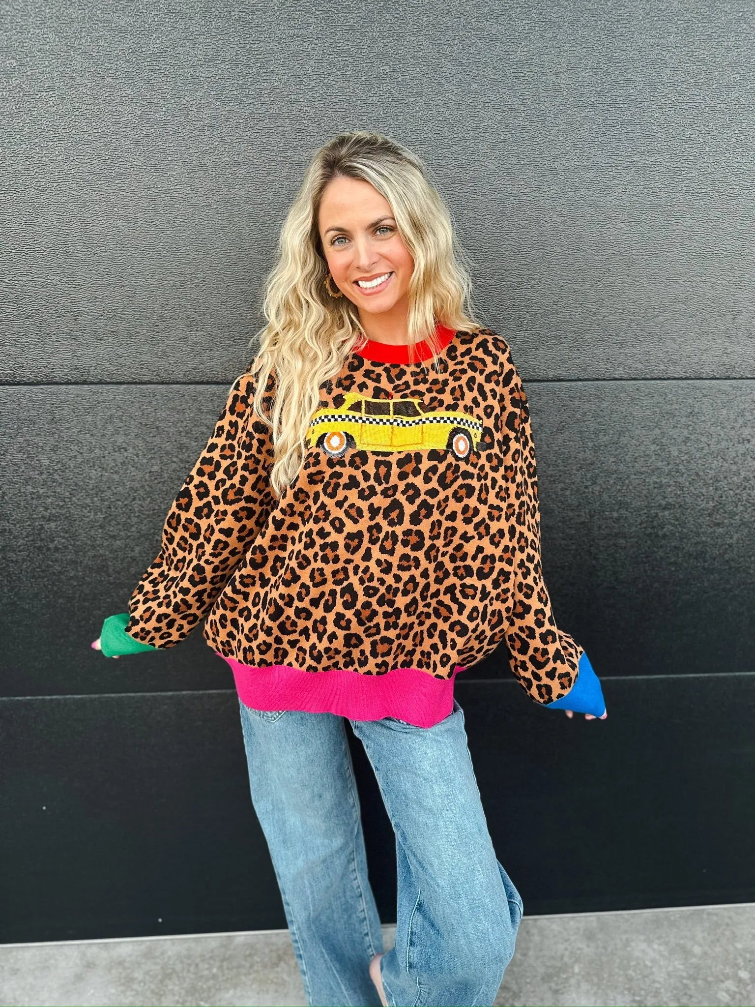 Woman wearing a leopard print sweater with a yellow taxi cab design, red collar, pink hem, and blue and green cuffs.