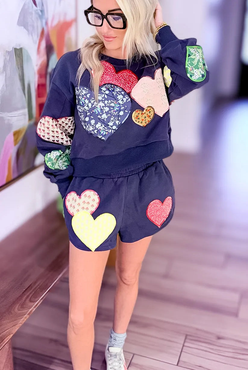 Navy jogger shorts and matching sweatshirt adorned with various colorful embroidered heart patches. Queen of Sparkles.