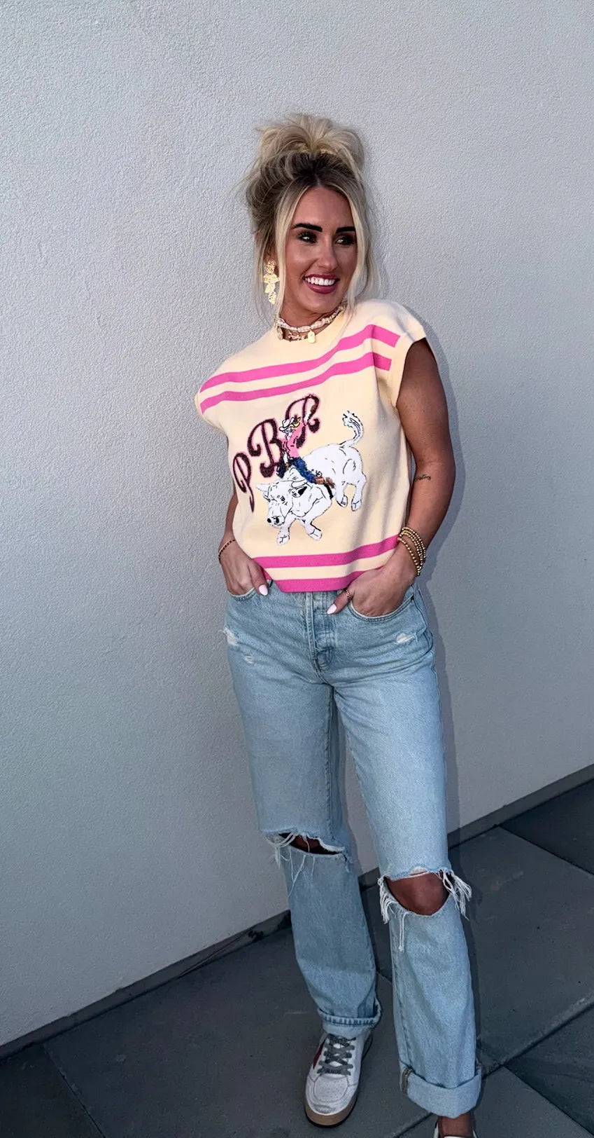 Queen of Sparkles tan knit tank top with pink stripes and a PBR bull rider graphic. Distressed light wash jeans.