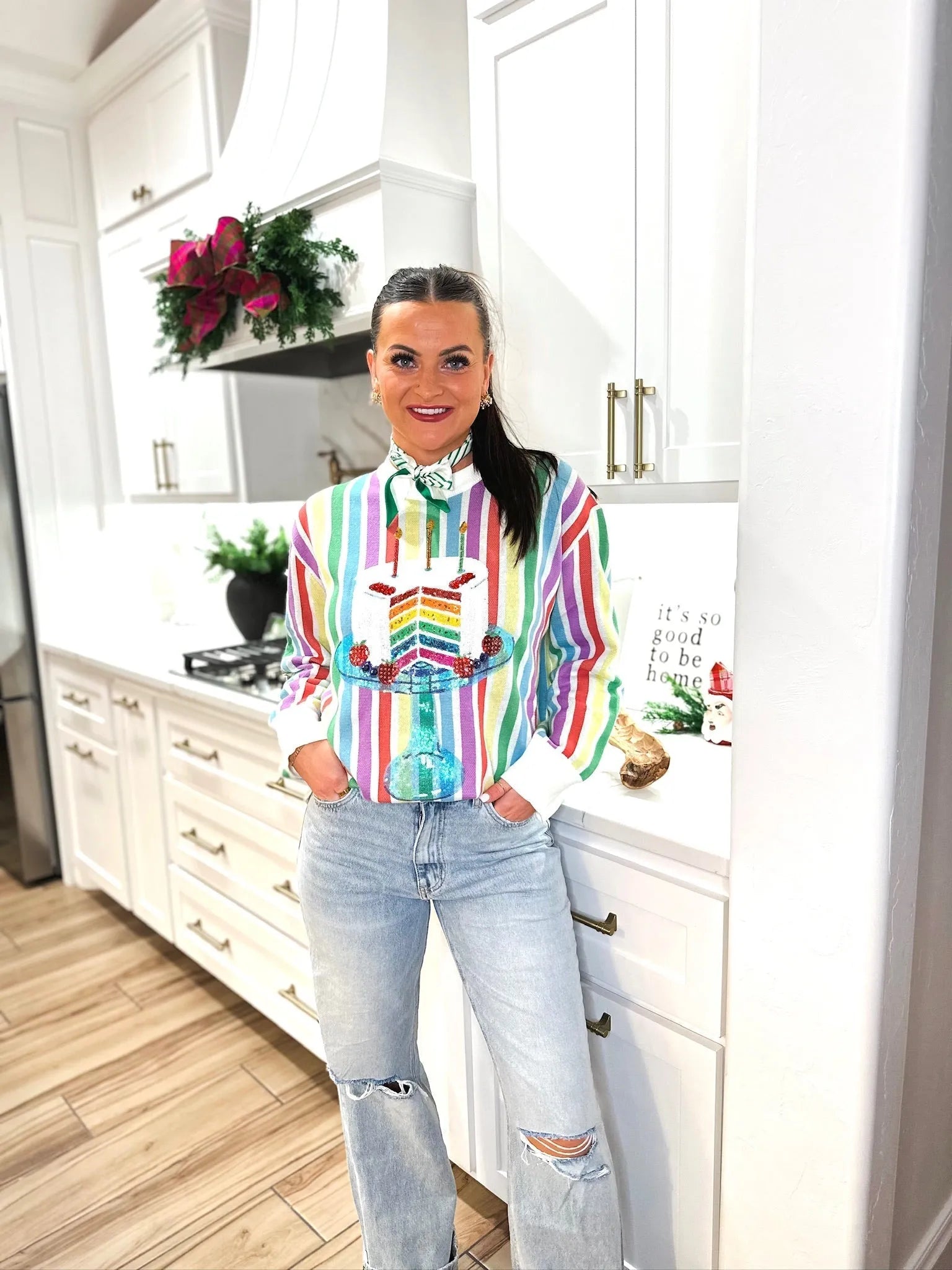 Woman in rainbow striped sweater featuring a sequined birthday cake graphic with candles and candles, paired with light