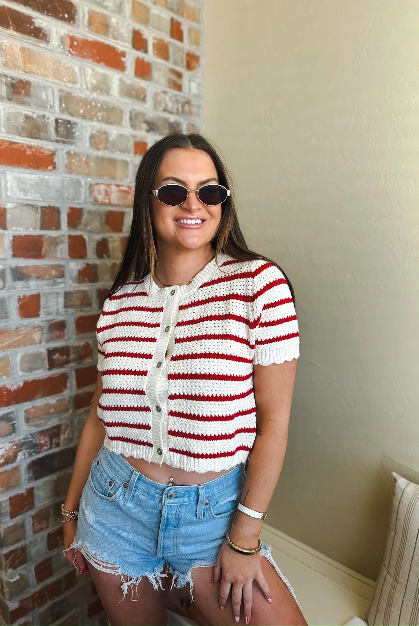 Cropped red and cream striped short sleeve button-down cardigan sweater with scalloped hem, worn by a woman with sunglasses