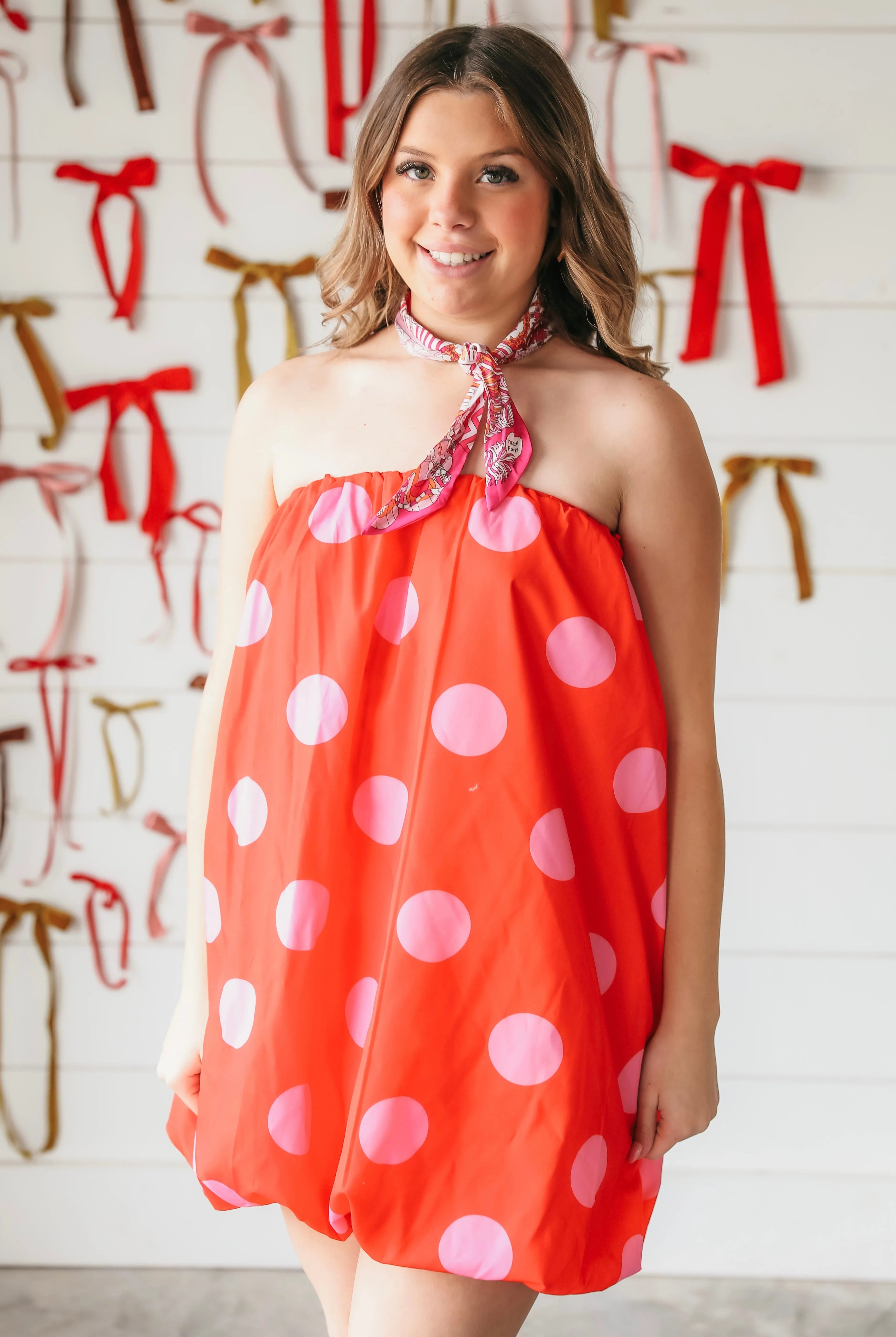 Strapless red bubble dress with large light pink polka dots, cinched at the neckline with a patterned scarf.