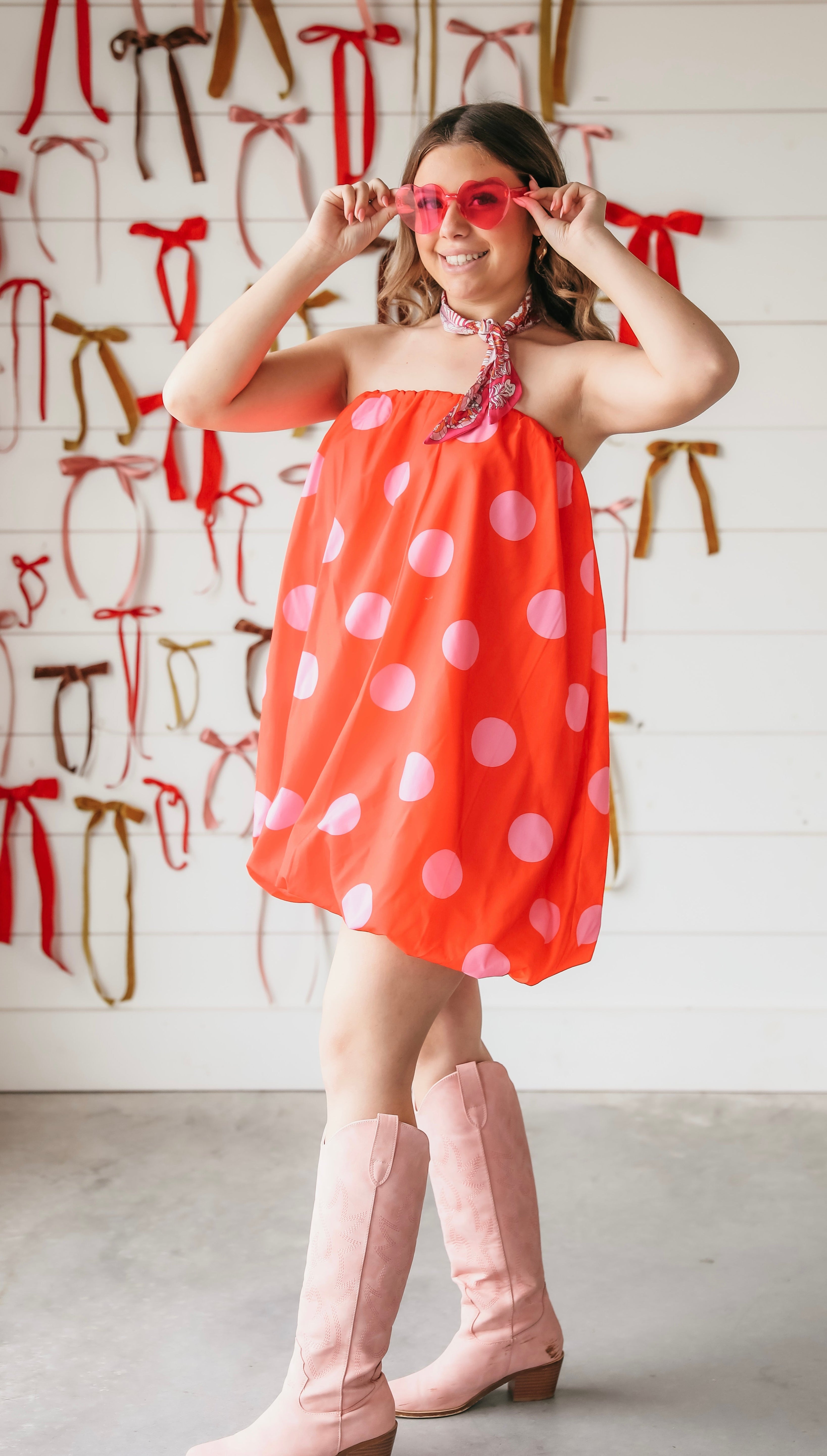 Red strapless bubble dress with large pink polka dots, worn by a woman with pink heart sunglasses and pink boots.